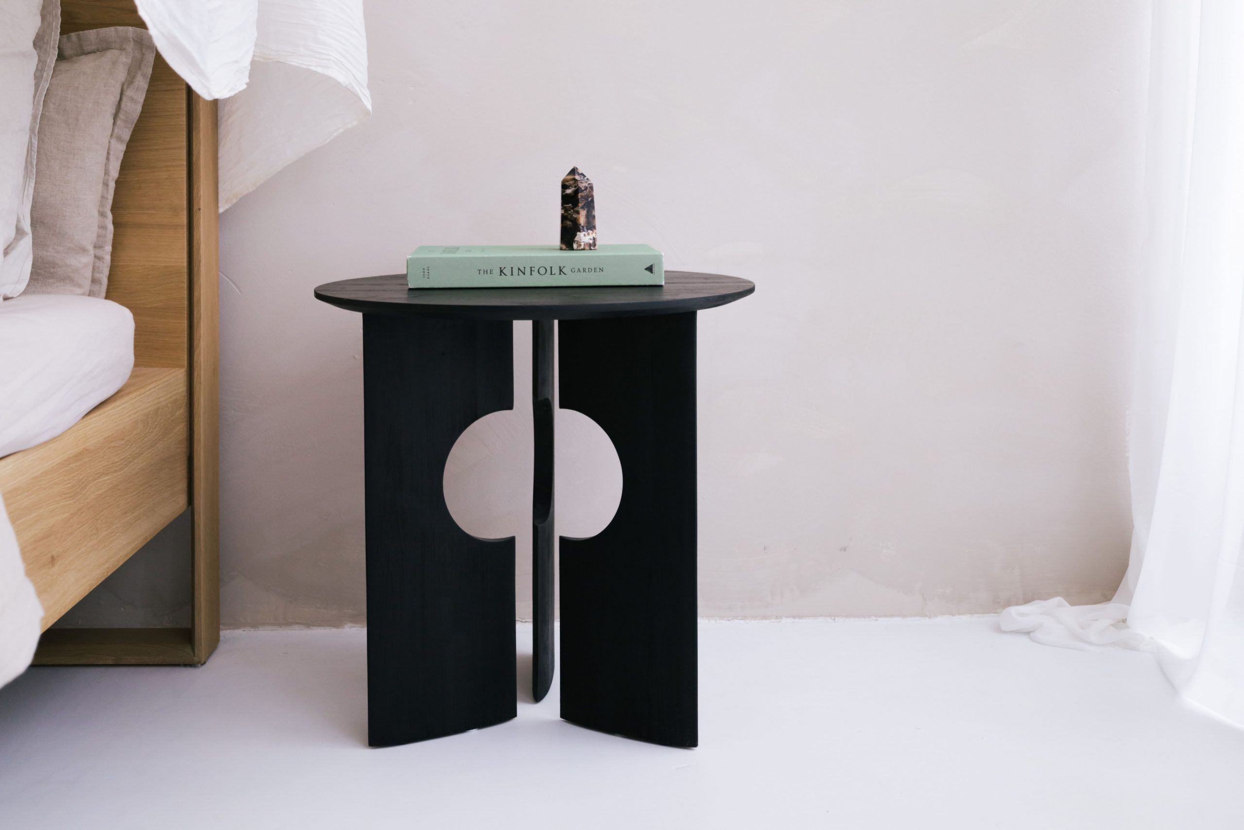 Contemporary bedroom featuring a black nightstand with a book and crystal decor in a minimalist setting.