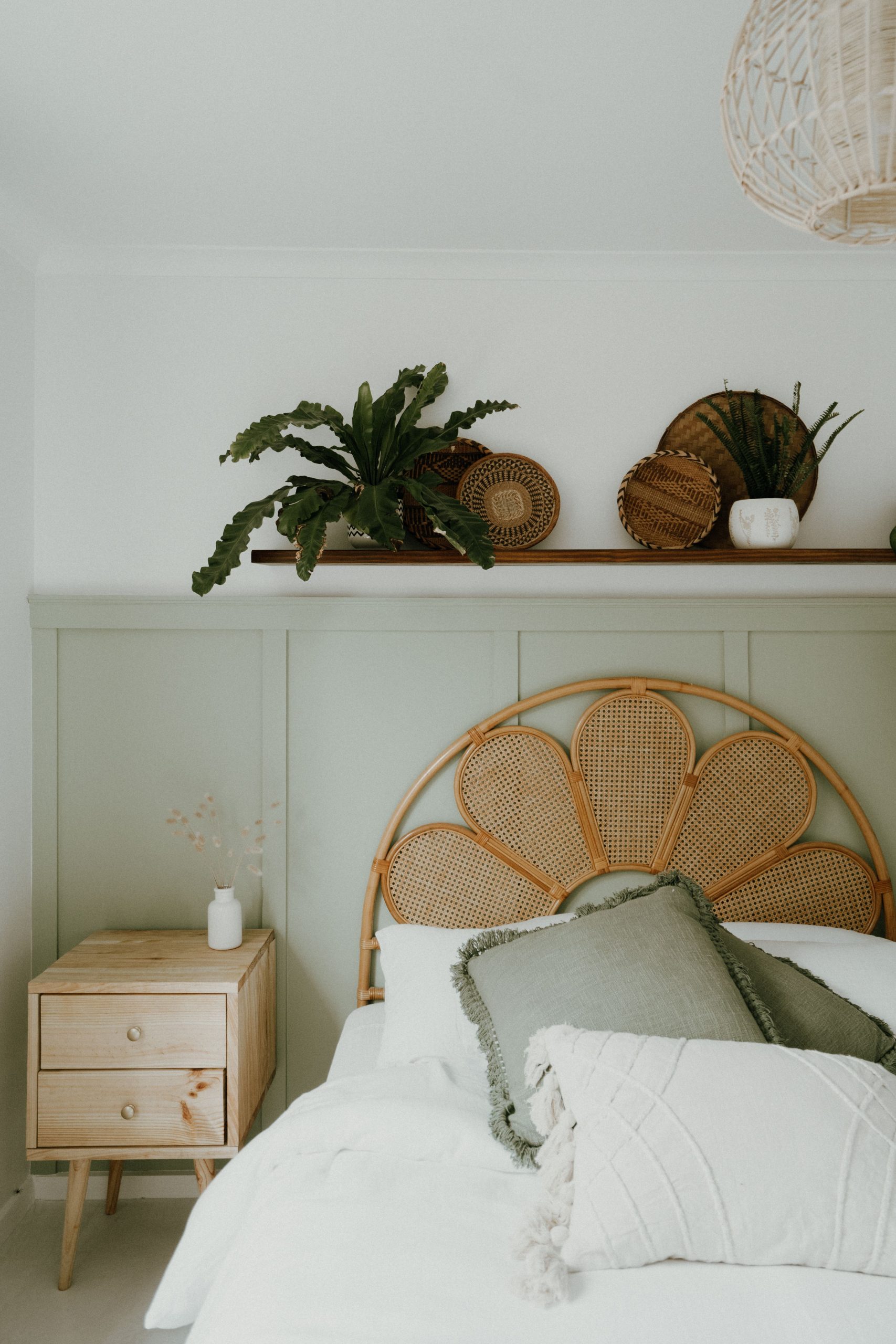 Cozy bedroom interior with wicker headboard and plants, highlighting Scandinavian design.