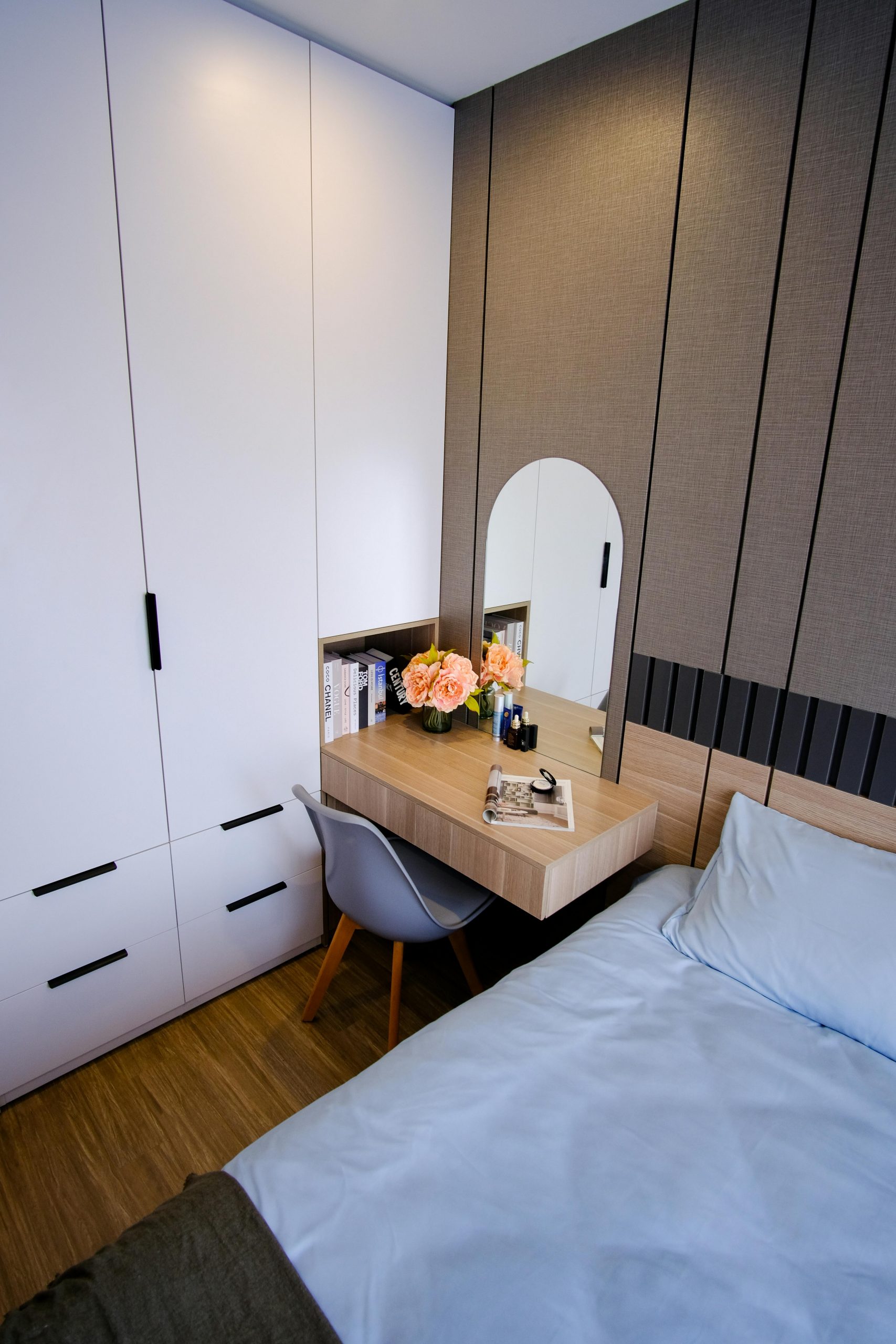 Cozy modern bedroom featuring a stylish vanity with mirror, books, and floral decor.
