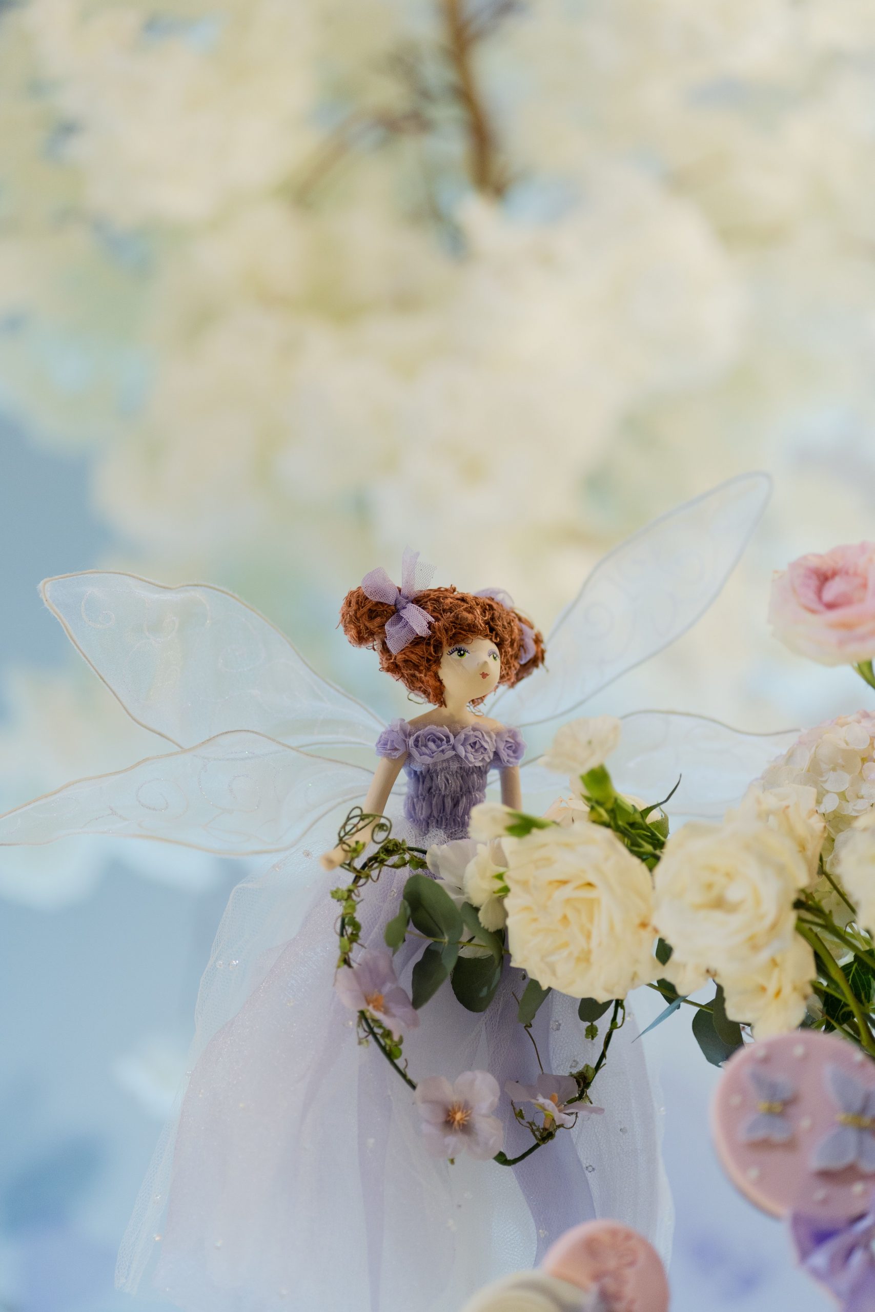 Delicate fairy doll adorned in purple amidst soft white blooms, creating a dreamy ambiance.