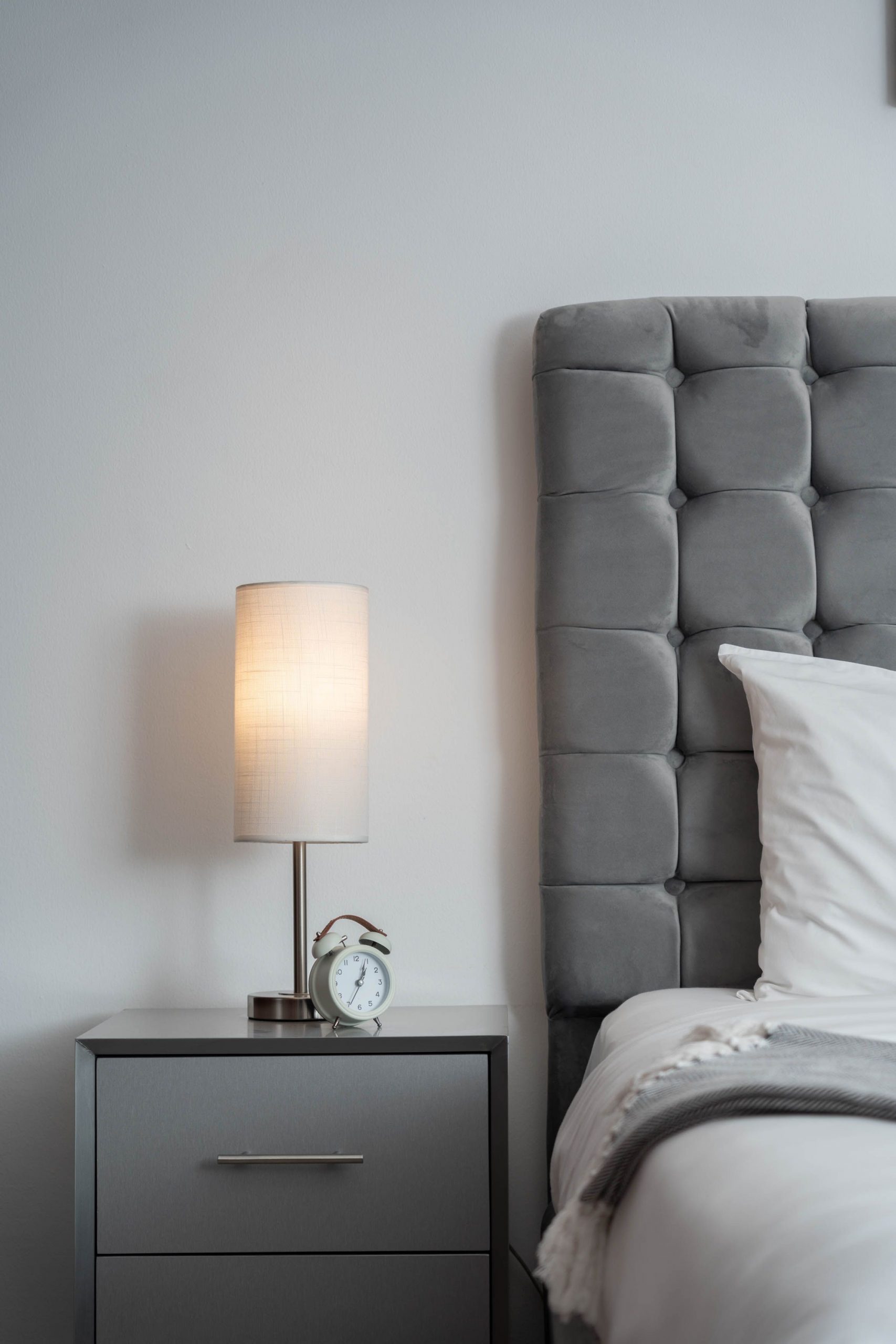 Elegant bedroom featuring a grey headboard, bedside lamp, and alarm clock on a nightstand.