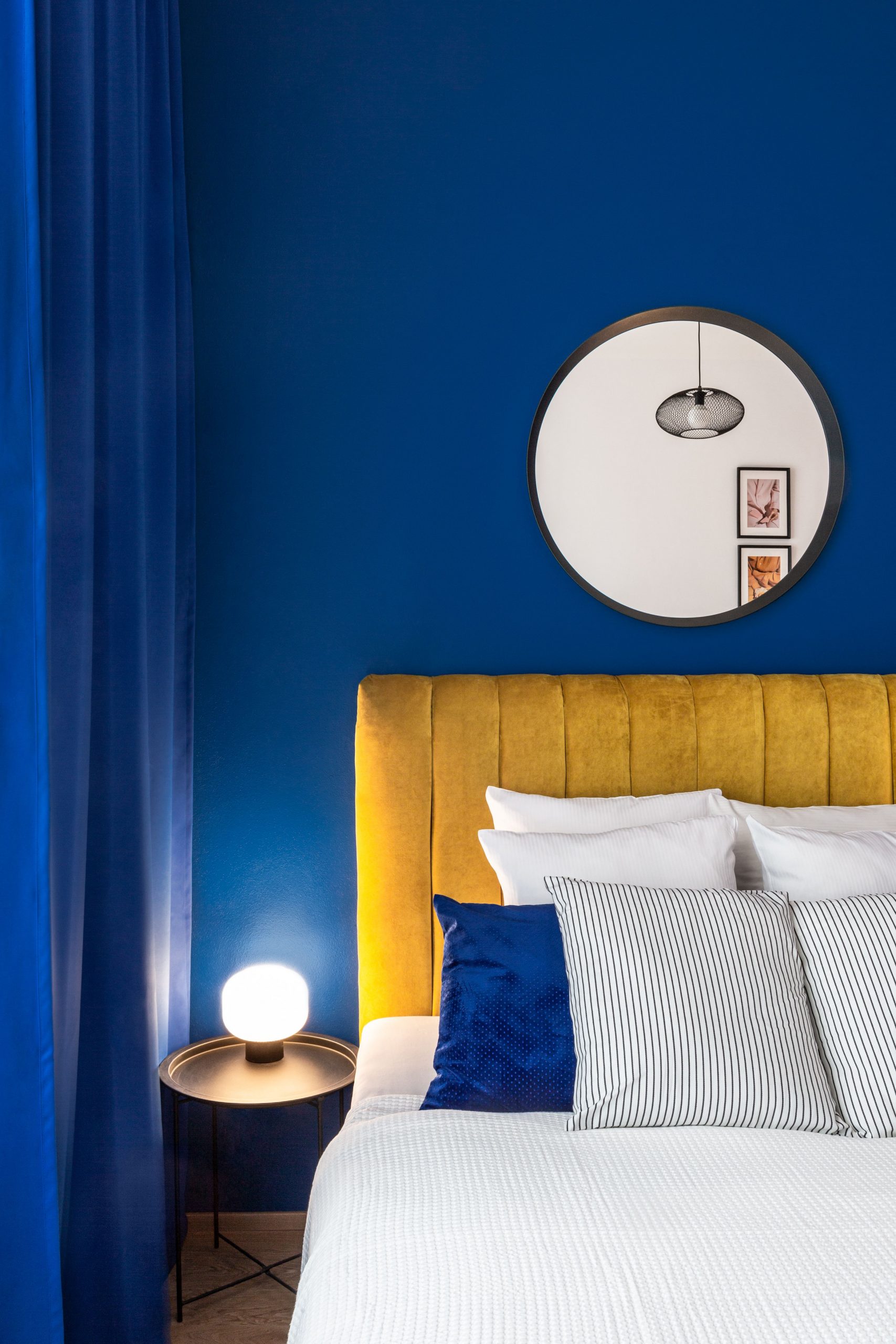 Elegant bedroom interior with blue walls, yellow headboard, and stylish decor.