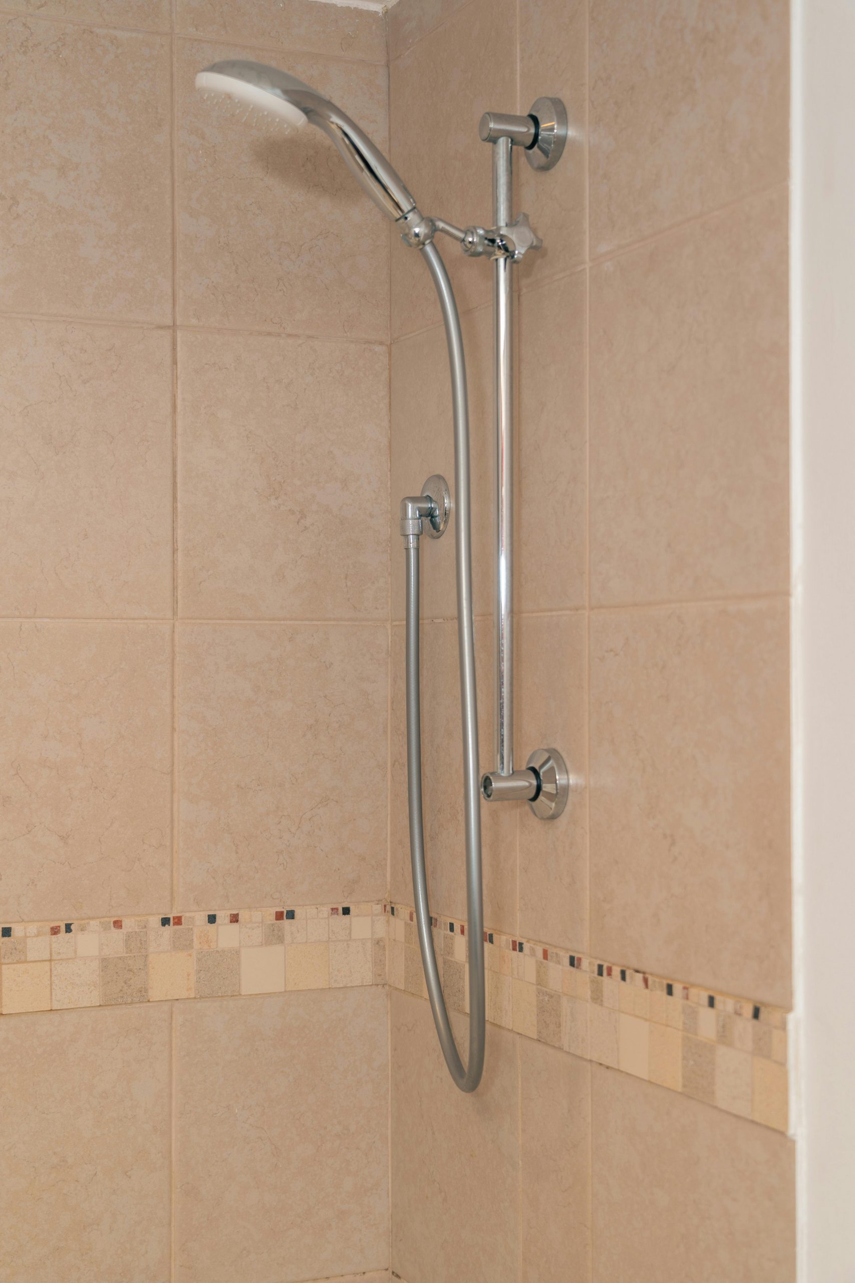 Elegant chrome showerhead and fixtures mounted on beige tiled shower wall.