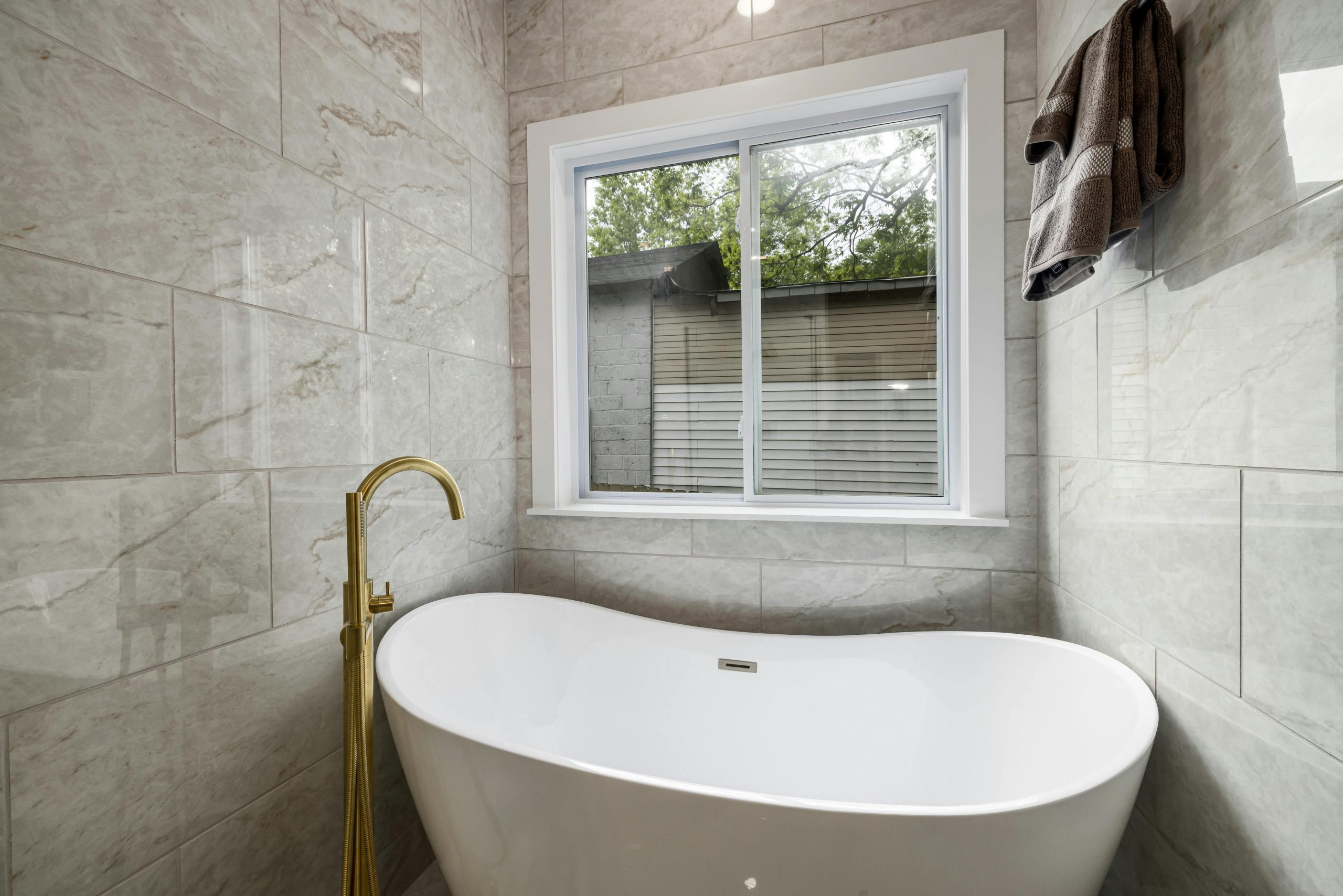 Elegant marble-walled bathroom featuring a freestanding white bathtub and a sleek window.
