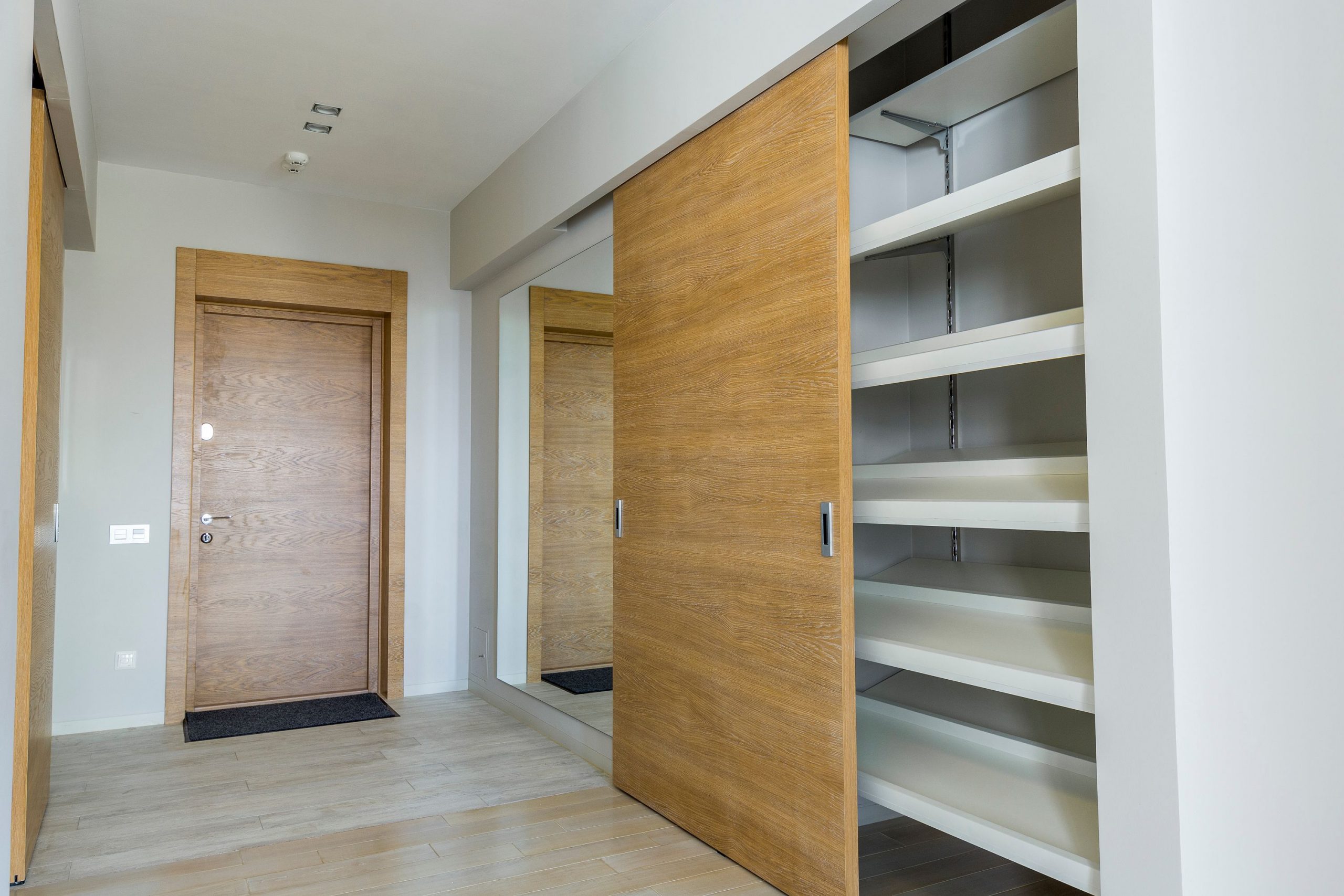 Elegant modern walk-in closet with wooden sliding door and empty shelves in a sleek minimalist style.