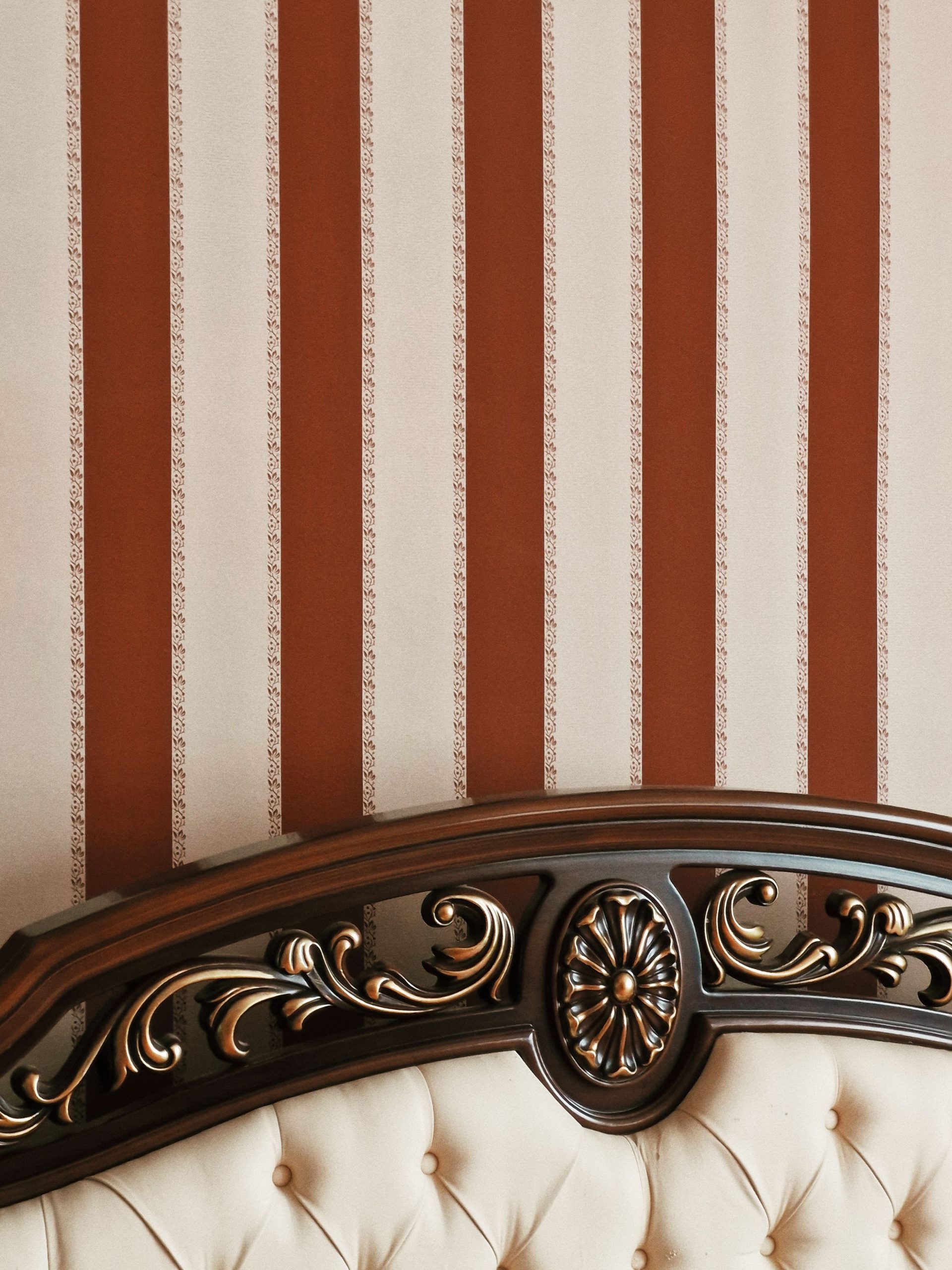 Elegant vintage headboard against a brown striped wall for classic interior decor style.