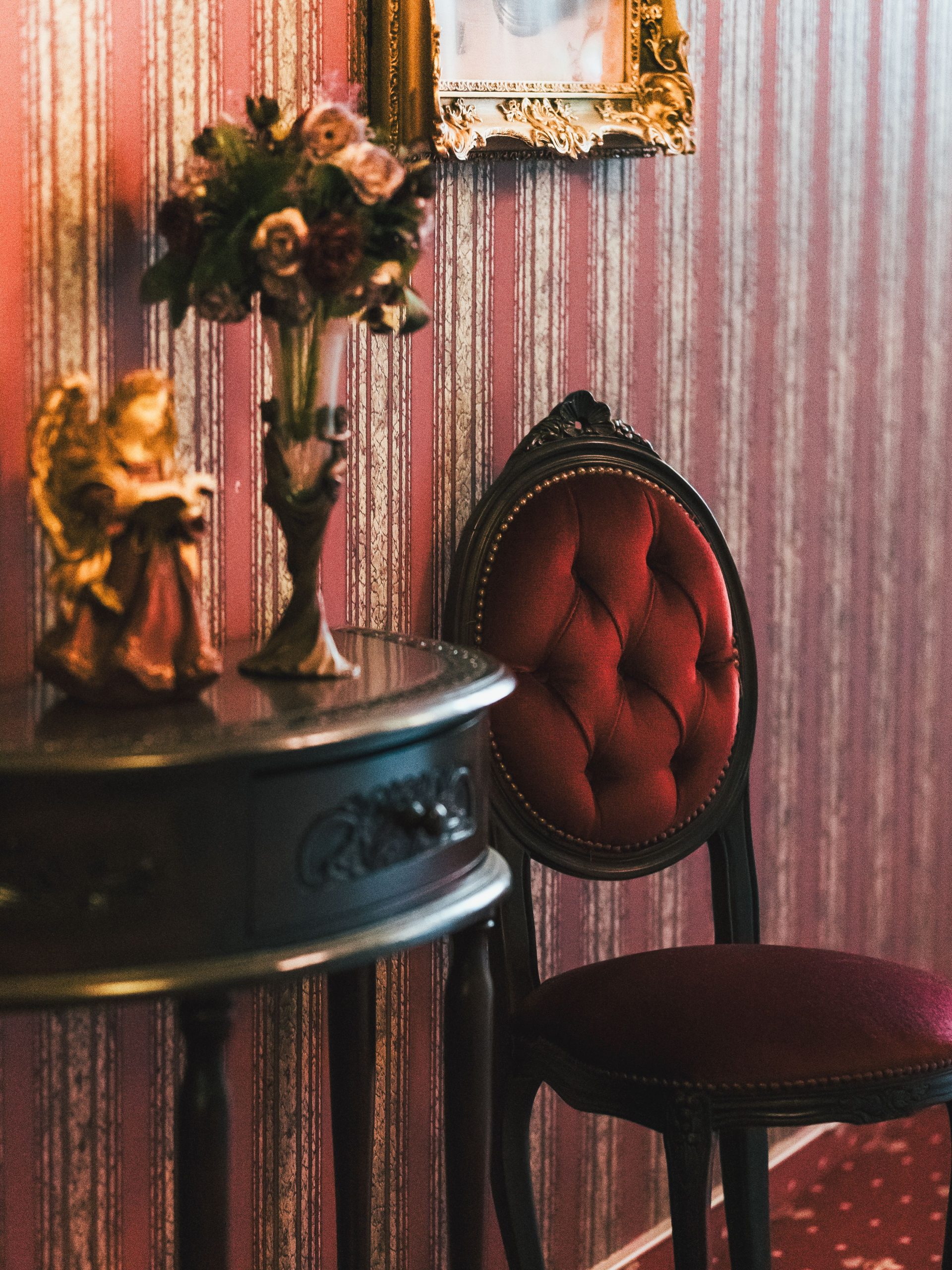 Elegant vintage interior with red velvet chair, floral arrangement, and ornate table.