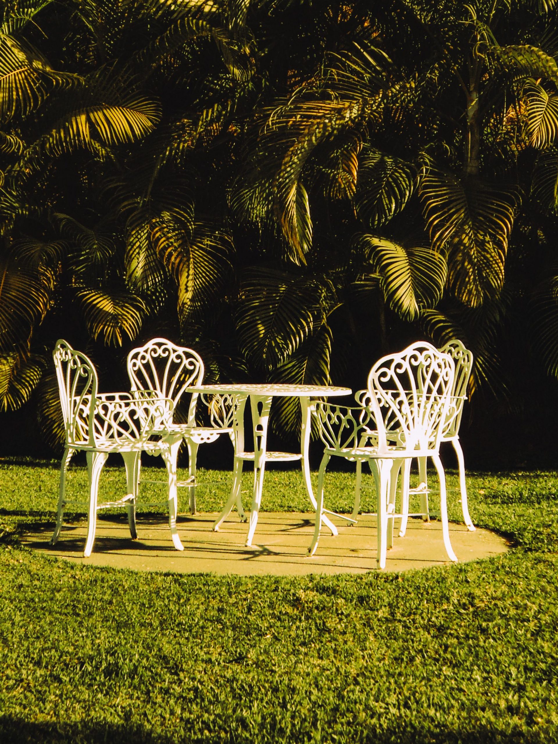 Elegant white iron chairs and table set on a green lawn, perfect outdoor relaxation spot.