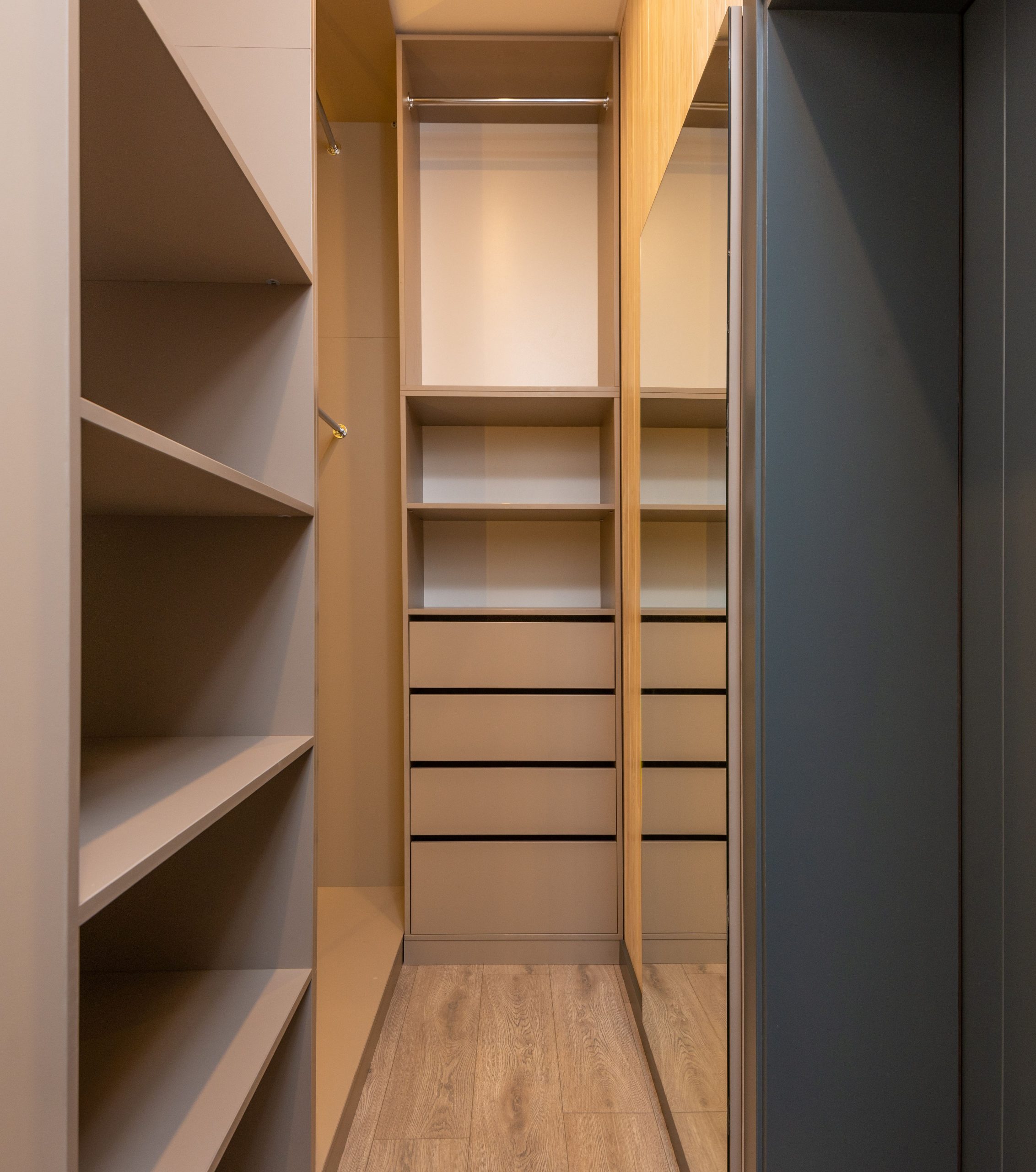 Empty shelves and racks in modern built in closet with wooden parquet floor and mirror hanging on wall