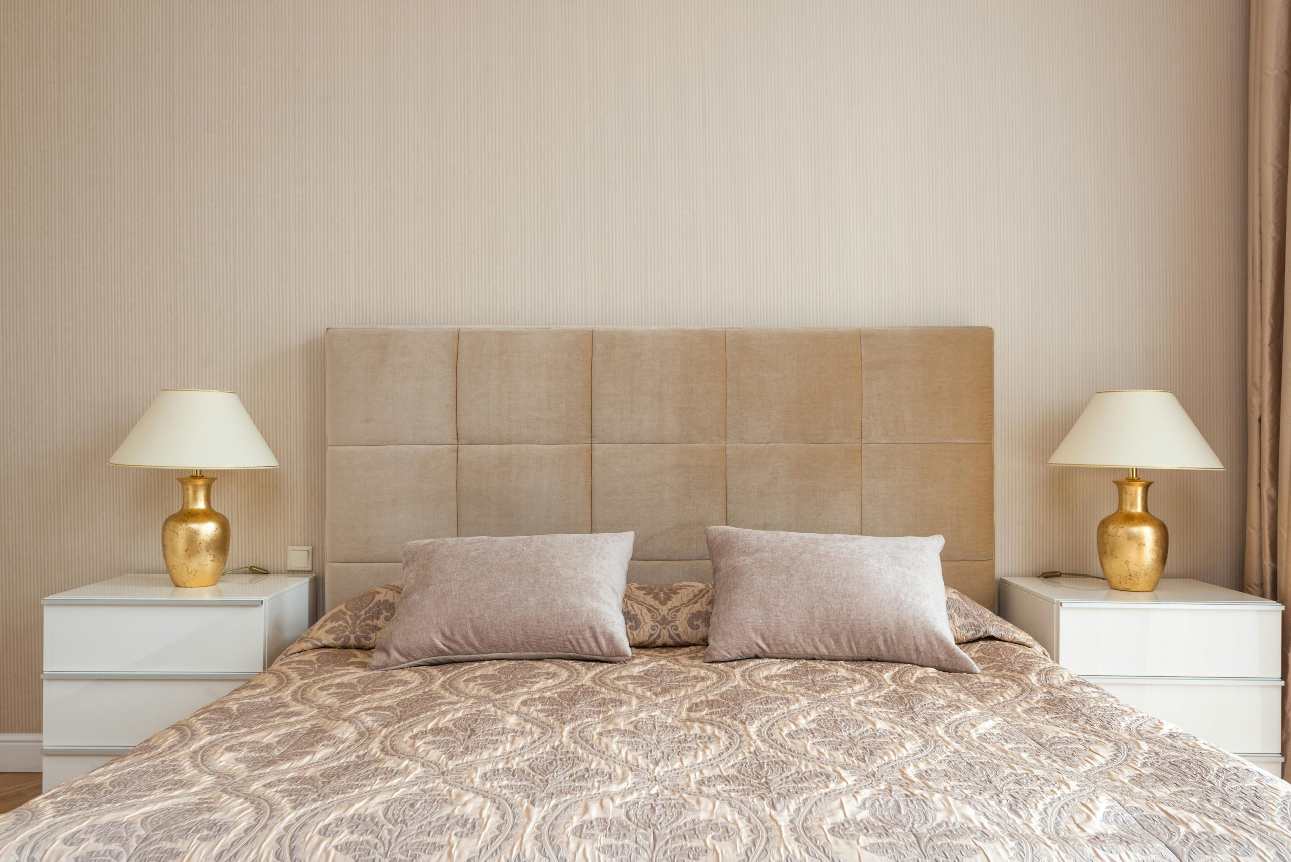 Interior of bedroom with big bed with soft headboard and lamps placed on nightstands in daylight