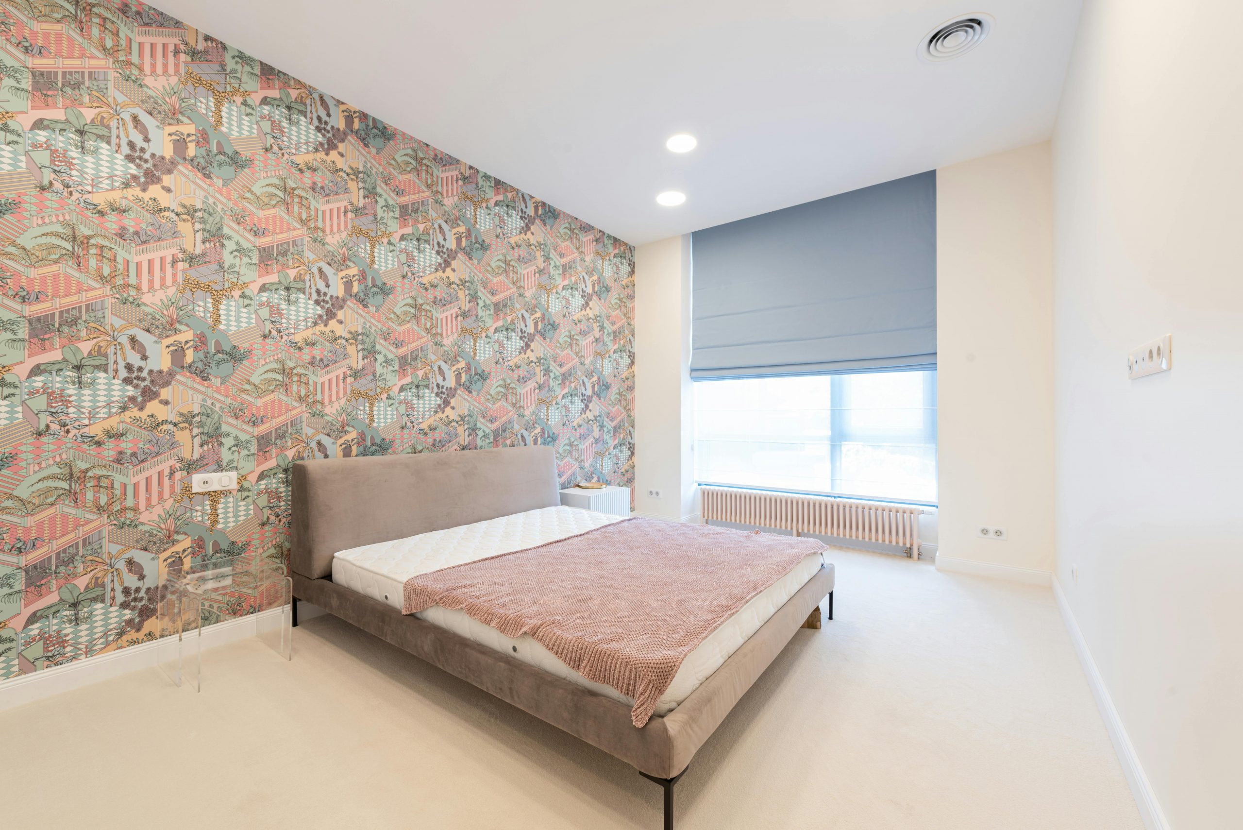 Interior of light apartment with bed near colorful wall and jalousie on window in daylight