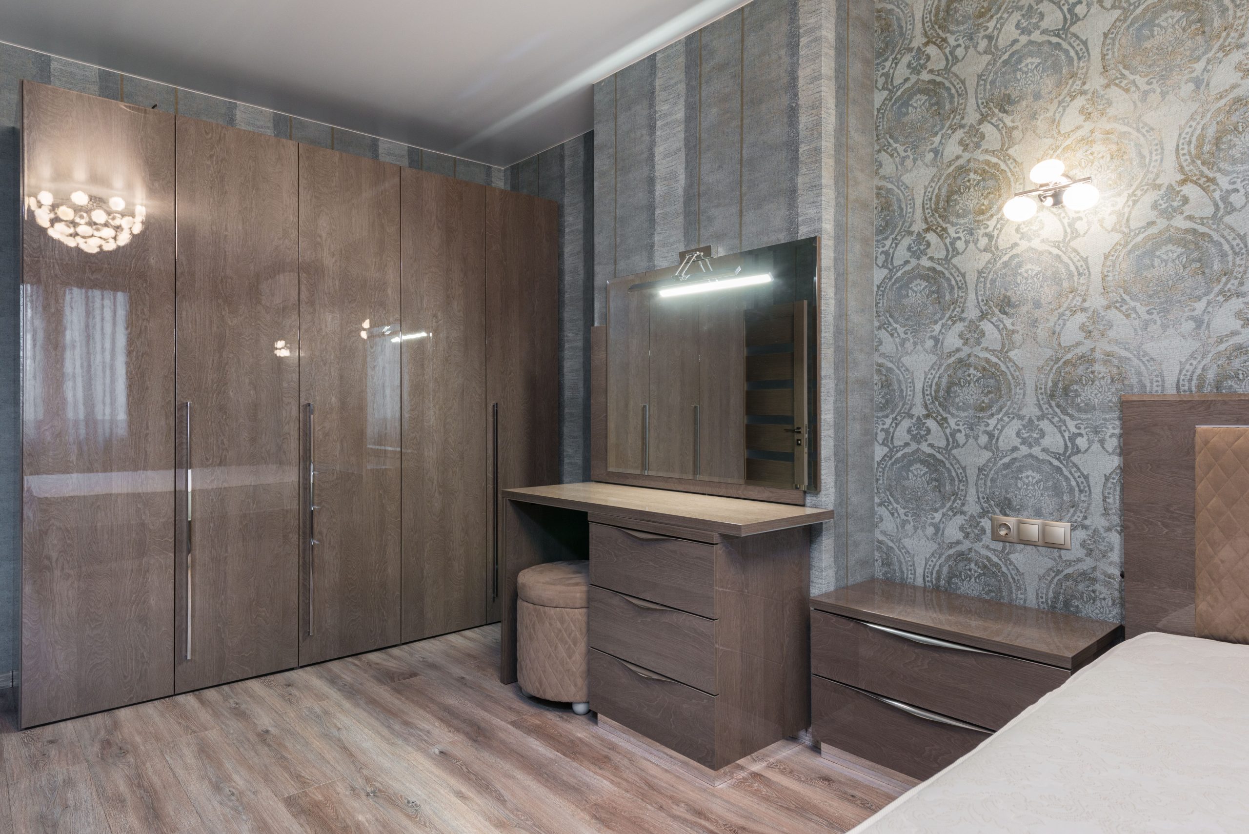 Interior of room with glossy cupboard with chest of drawers with mirror and nightstand near bed