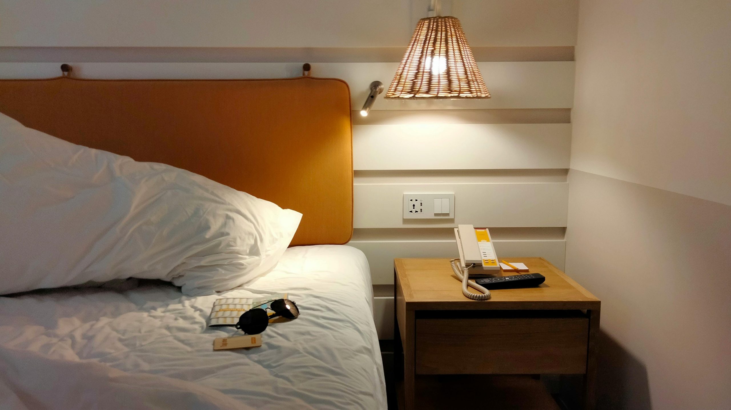 Inviting bedroom space with a lamp-lit nightstand, phone, and sunglasses on the bed.