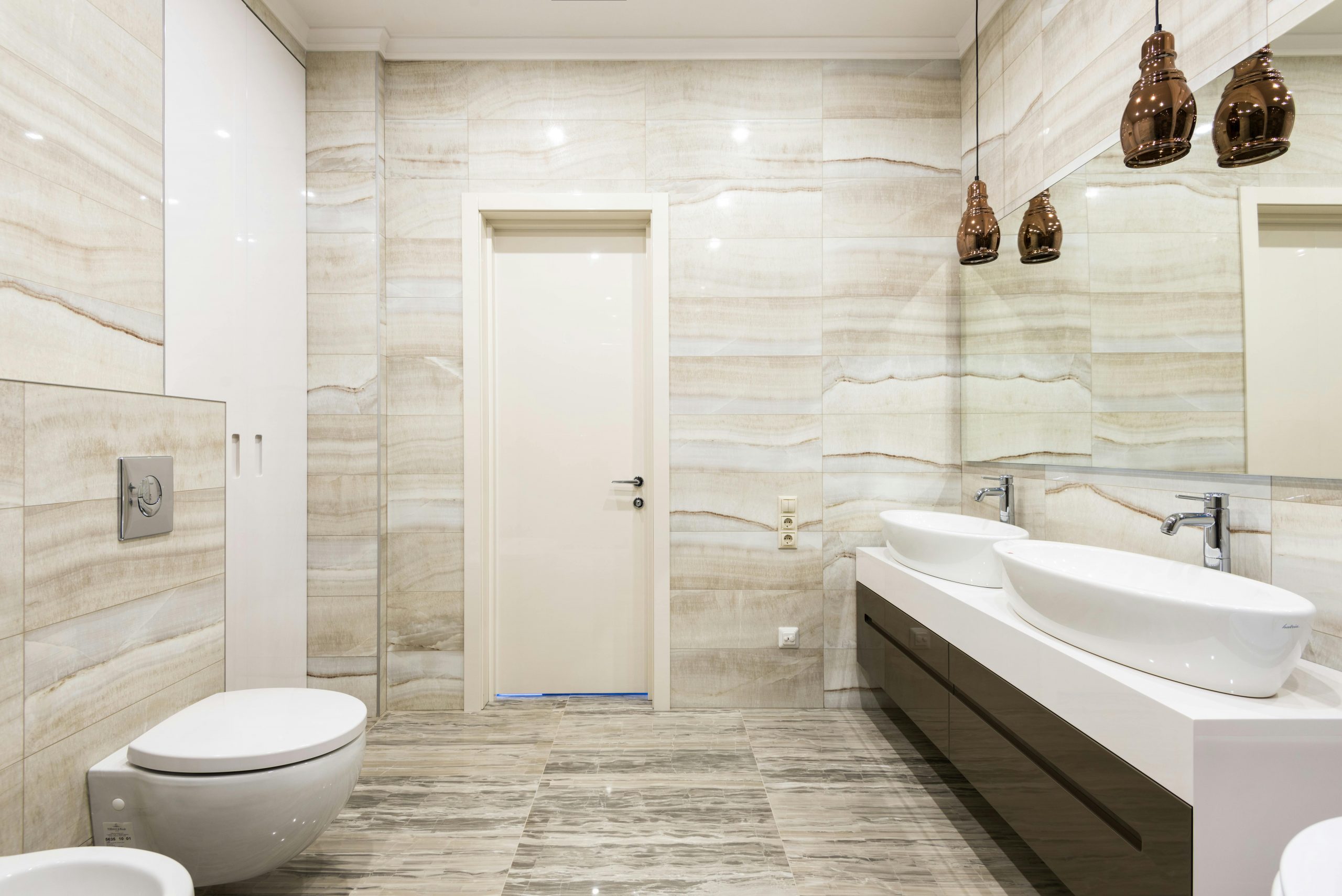 Luxurious bathroom featuring dual sinks, mirrors, and sleek design with beige tiles.