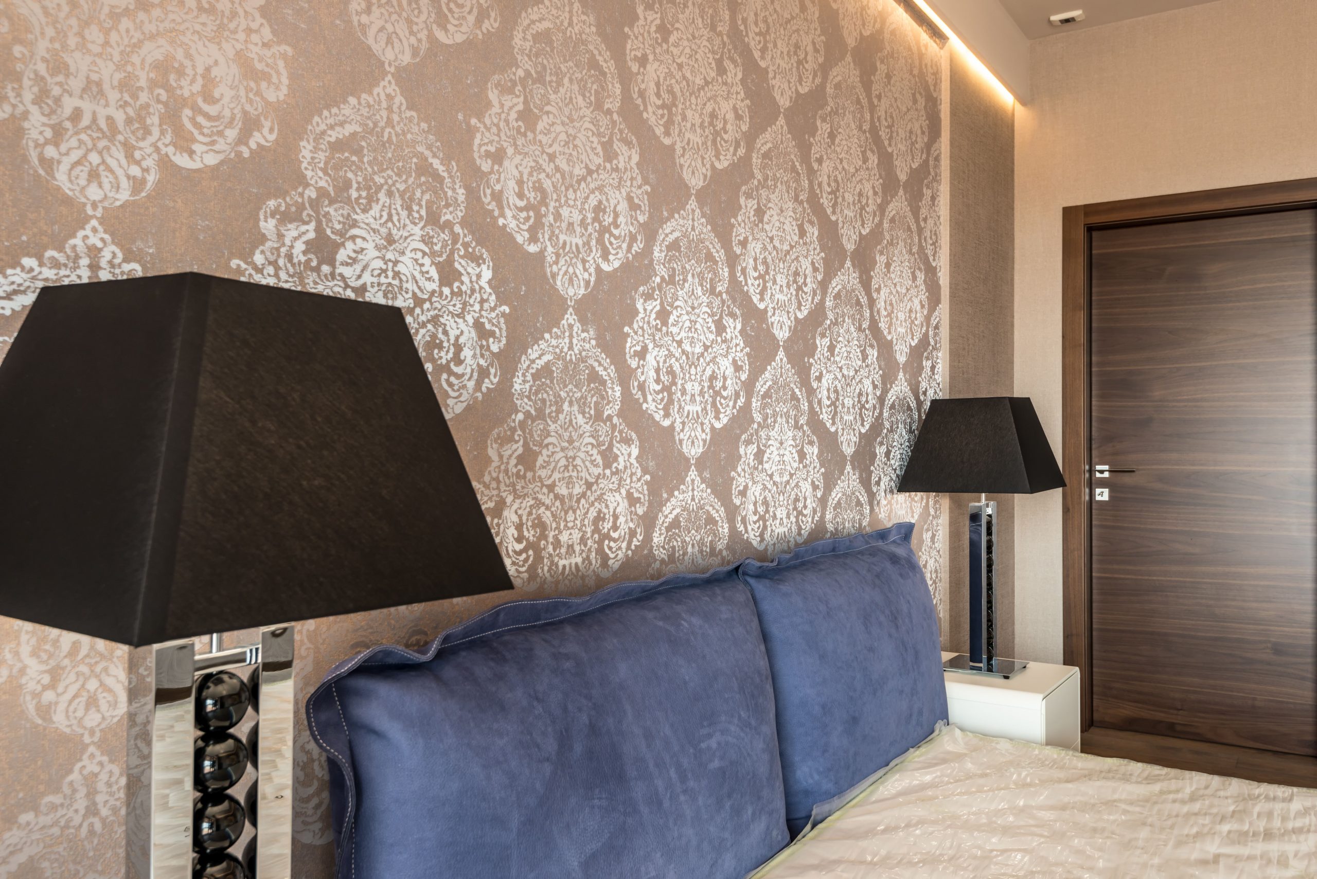 Modern bedroom with elegant wallpaper design, blue pillows, and stylish black lamps.