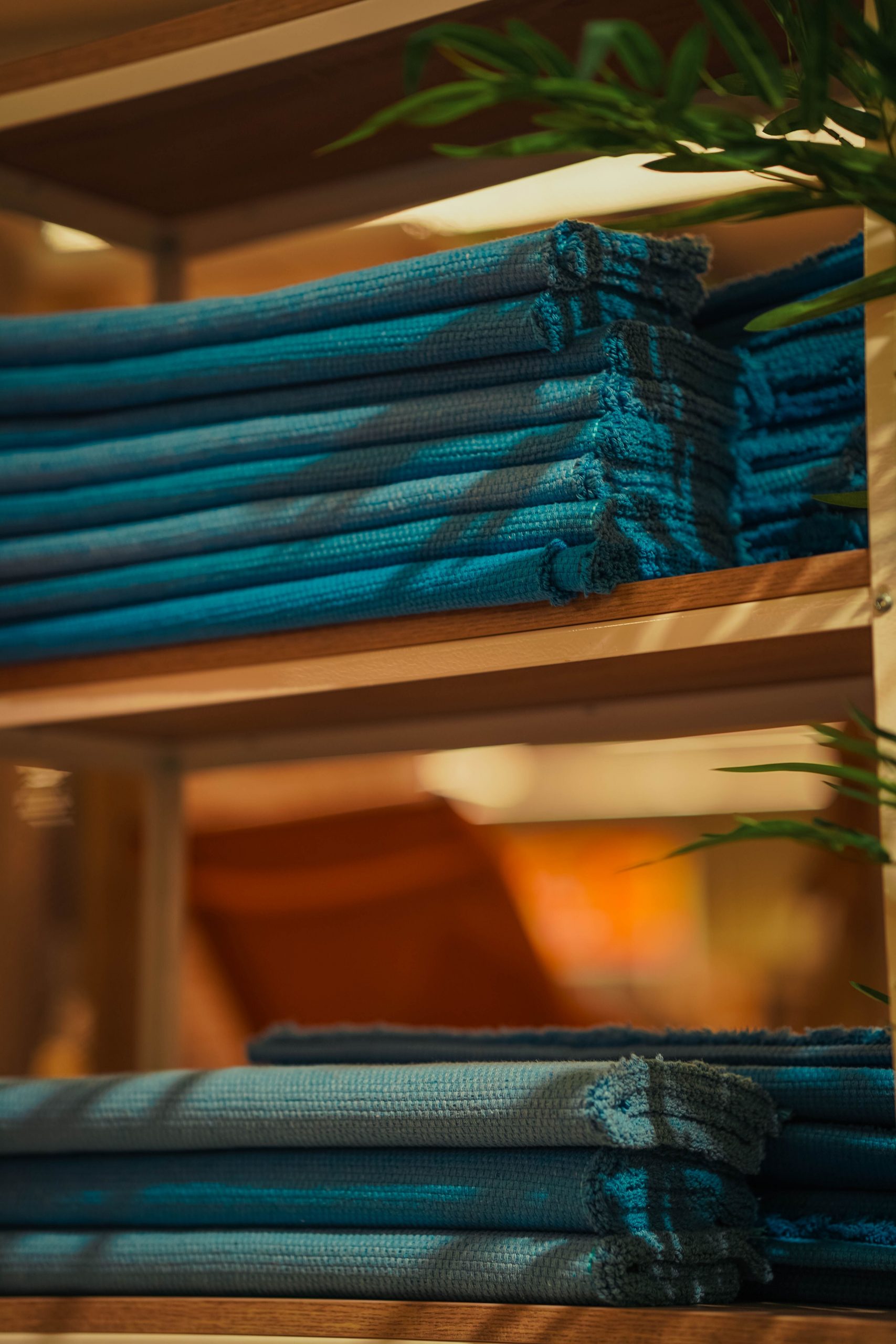 Neatly folded stack of blue towels on a wooden shelf with soft lighting.