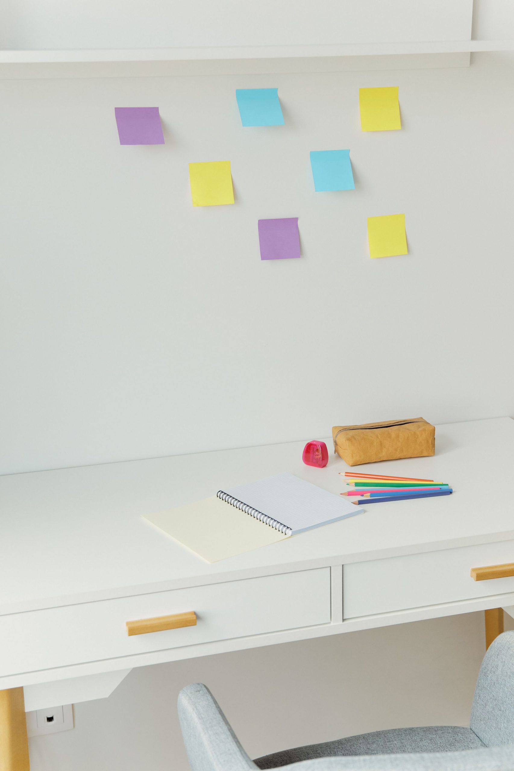 Organized minimalist desk setup with colorful pencils, a notebook, and sticky notes on a white background.