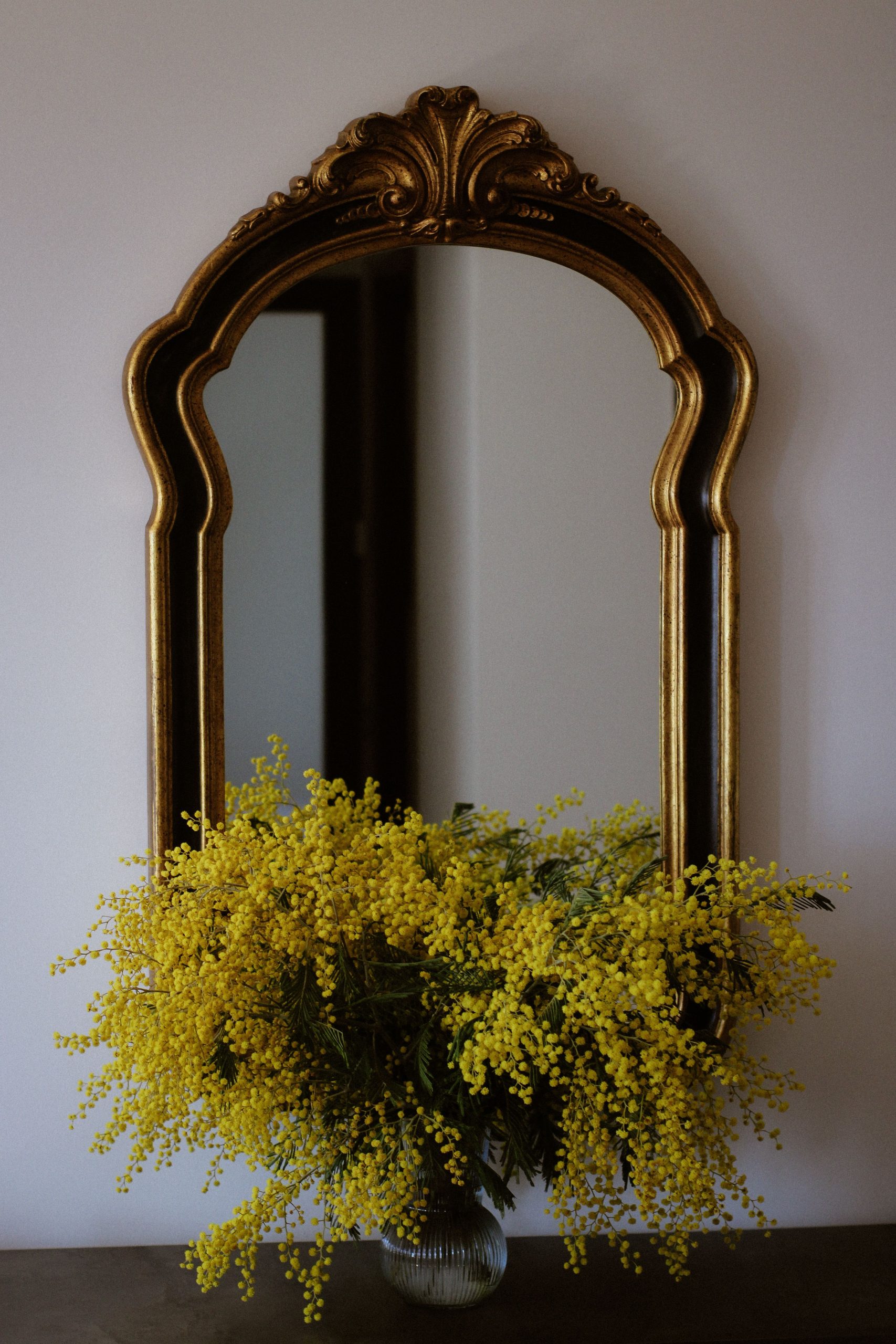 Ornate gold mirror reflecting vibrant yellow floral arrangement indoors.