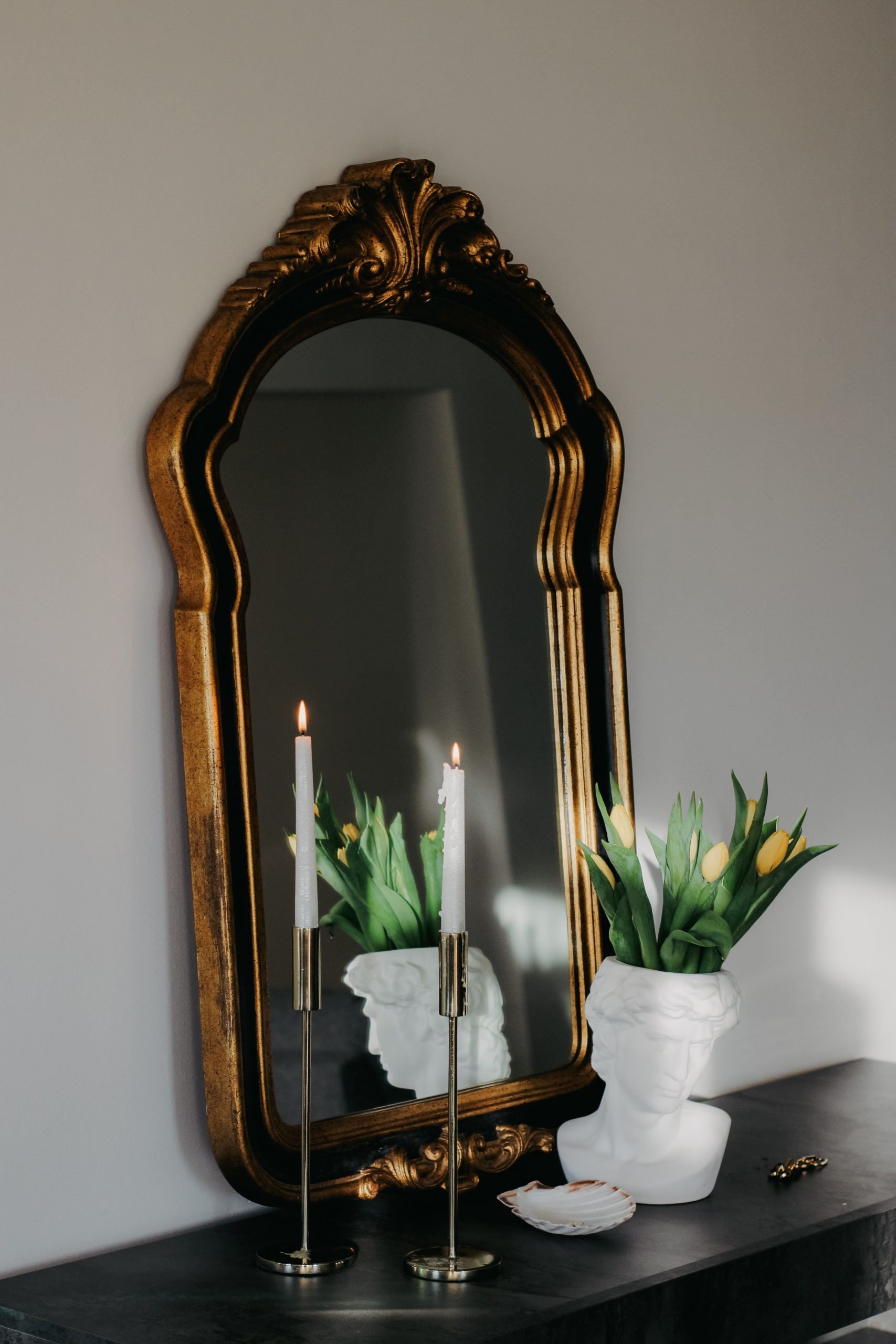Refined interior decor with ornate mirror, candles, and floral bust on a table.