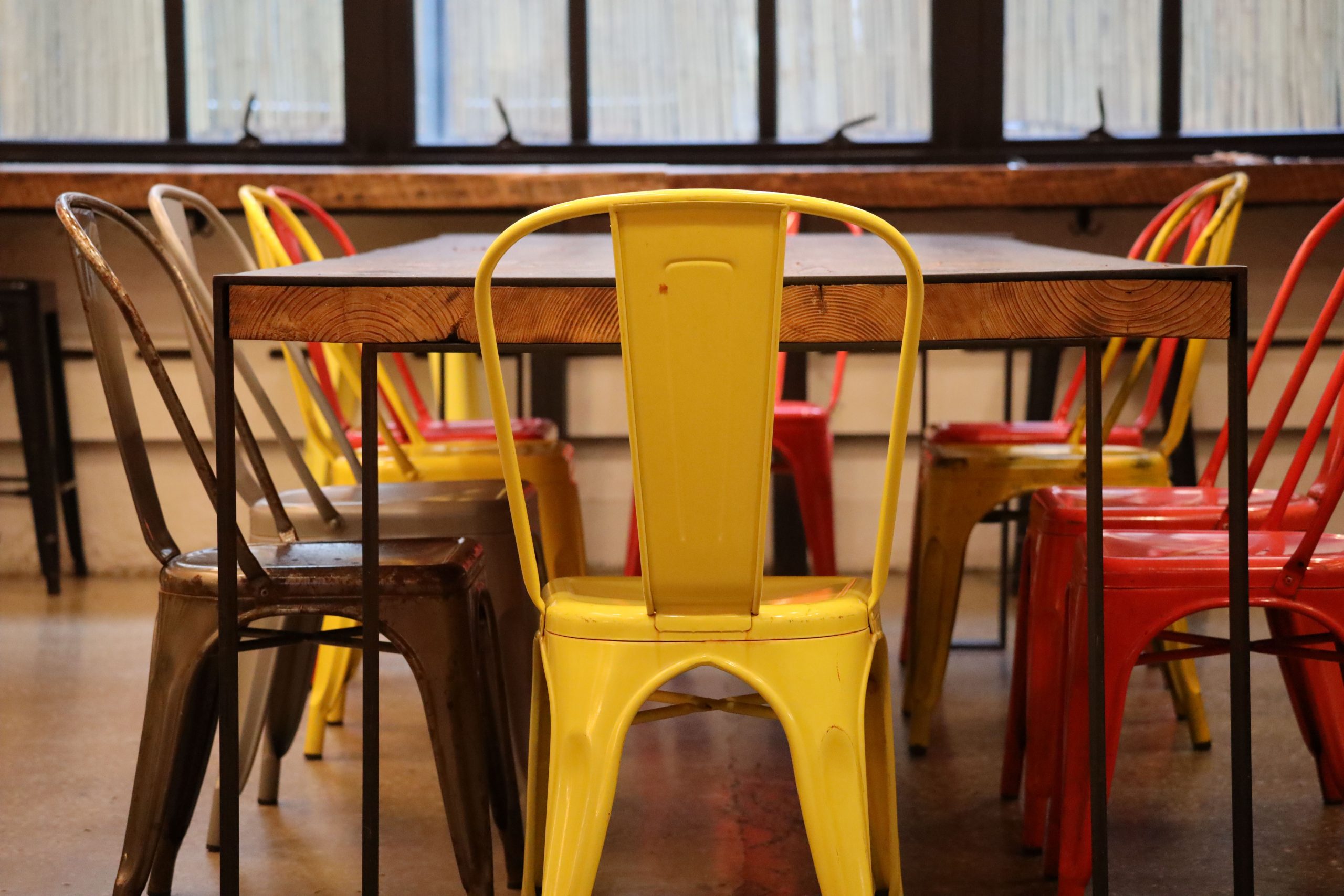 Retro industrial chairs in vibrant colors around a wooden table, indoor loft setting.