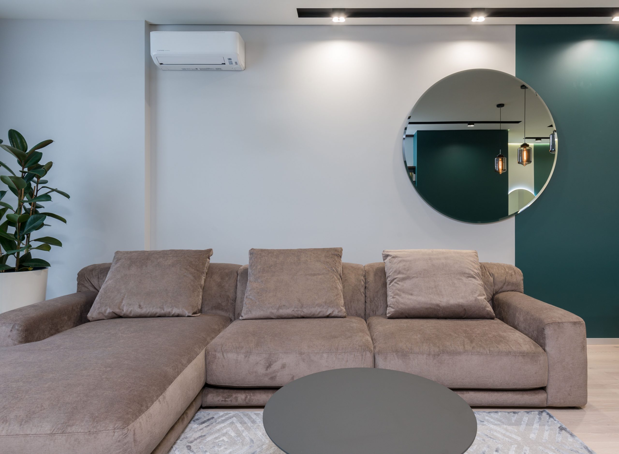 Round mirror hanging on wall above big comfortable sofa in spacious living room of modern apartment