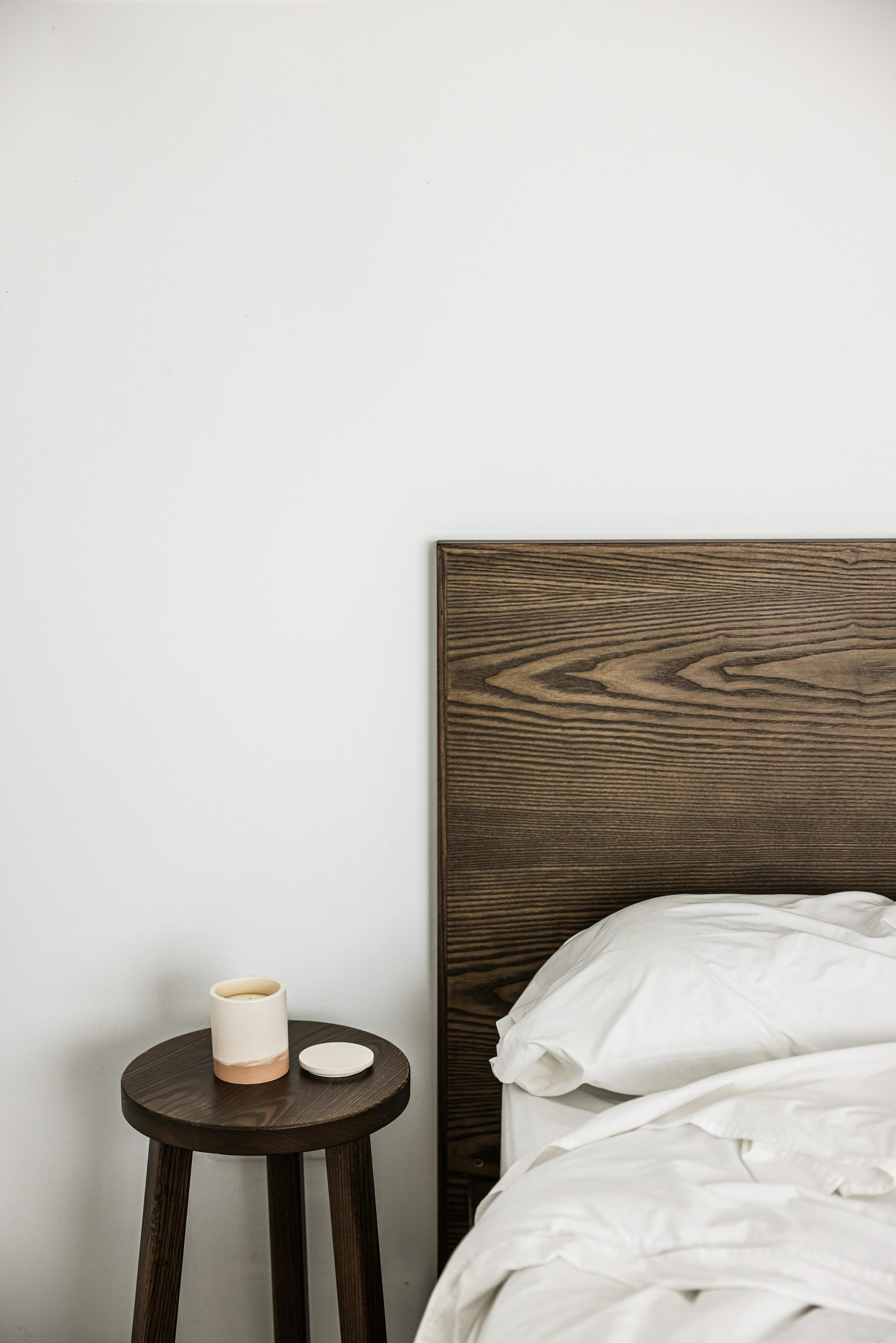 Simple bedroom setup featuring a wooden headboard and bedside table with a mug.