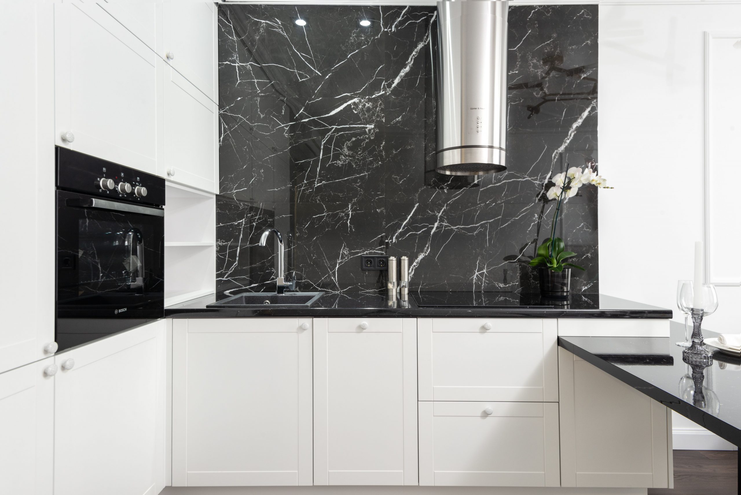 Sleek contemporary kitchen featuring white cabinets and black marble backsplash for a clean, minimalistic design.