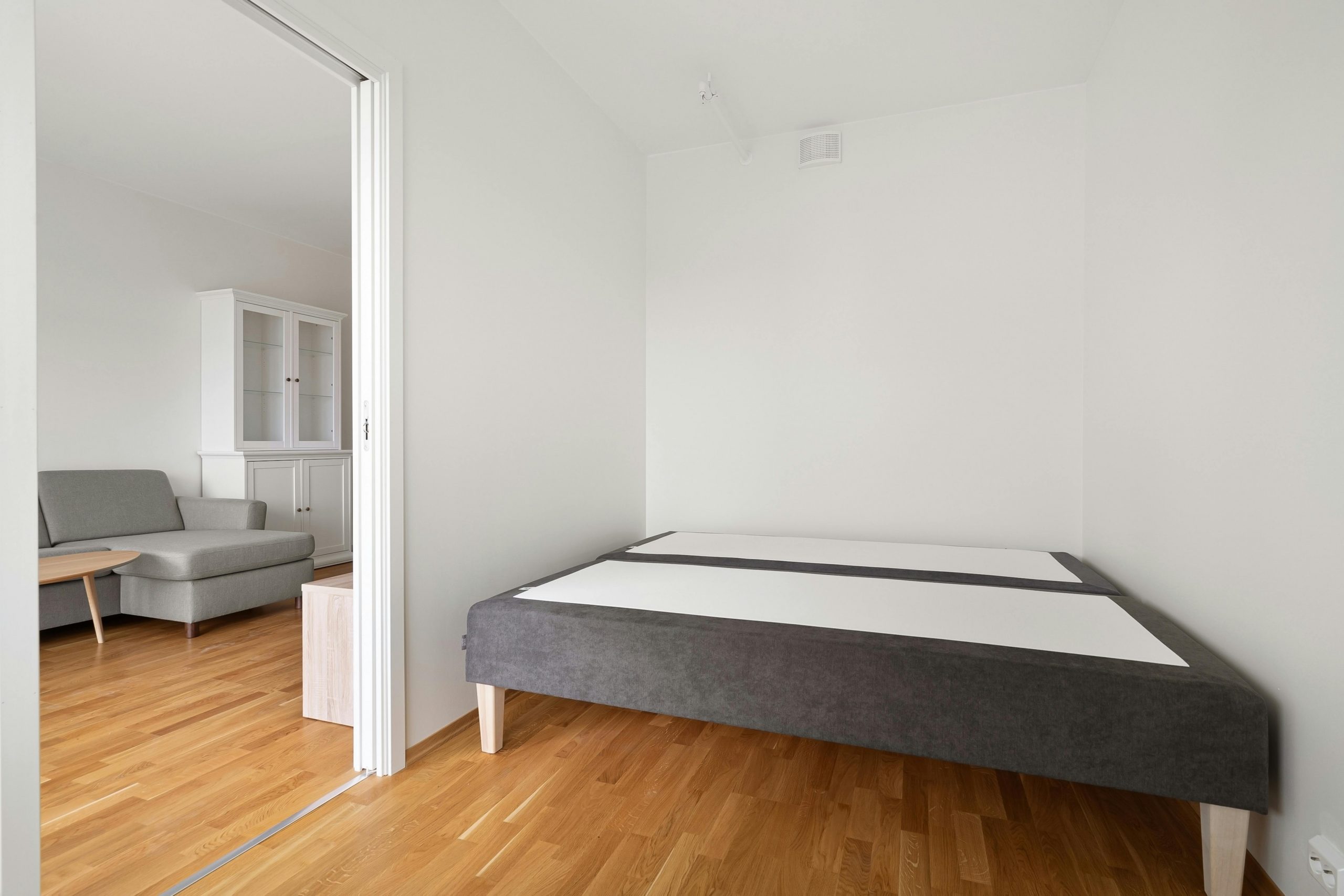 Spacious minimalist bedroom featuring a modern sofa and bed frame with wooden parquet flooring.