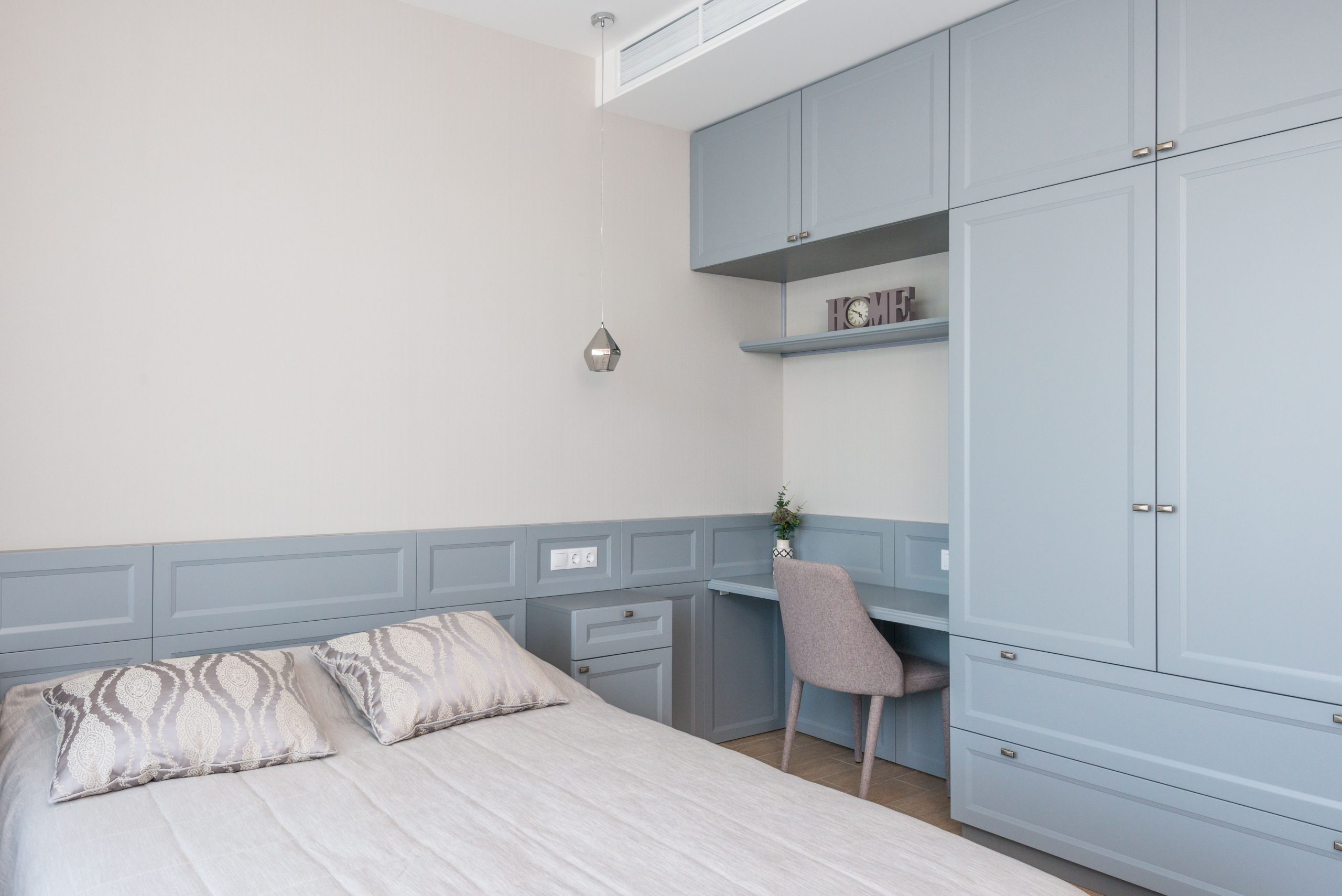 Stylish bedroom features built-in cabinetry, soft blue tones, and a cozy workspace.