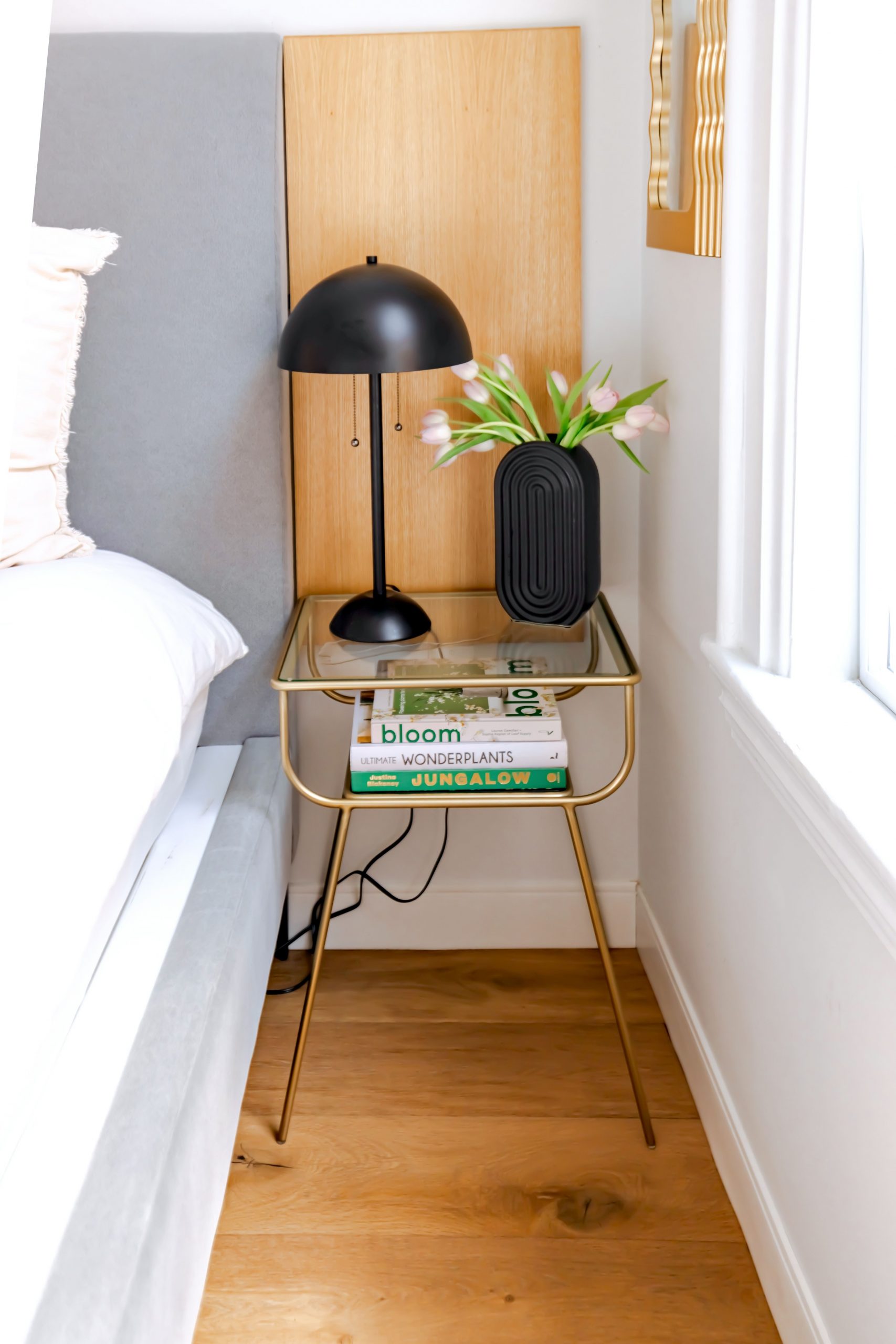 Stylish bedroom nightstand with a black lamp, books, and a vase of flowers.