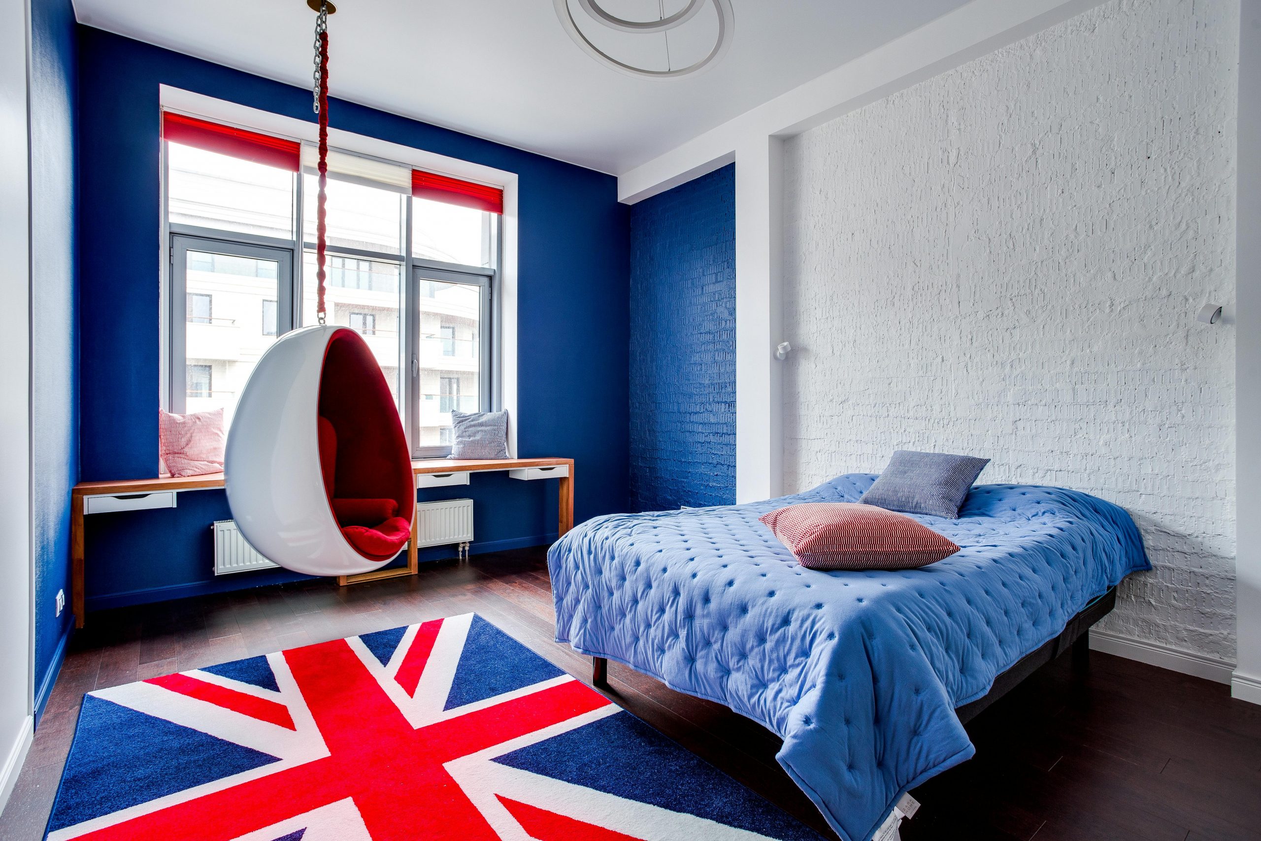 Stylish bedroom with Union Jack rug, hanging chair, and blue decor theme.