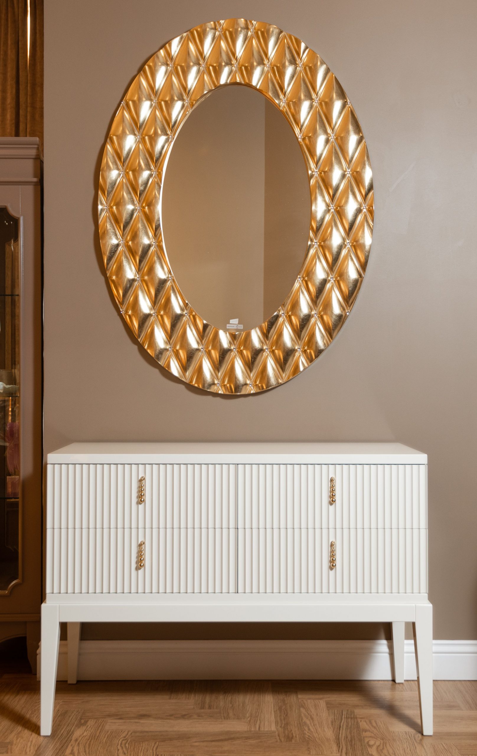 Stylish interior design featuring a gold ornate mirror above a sleek white cabinet against a neutral wall.
