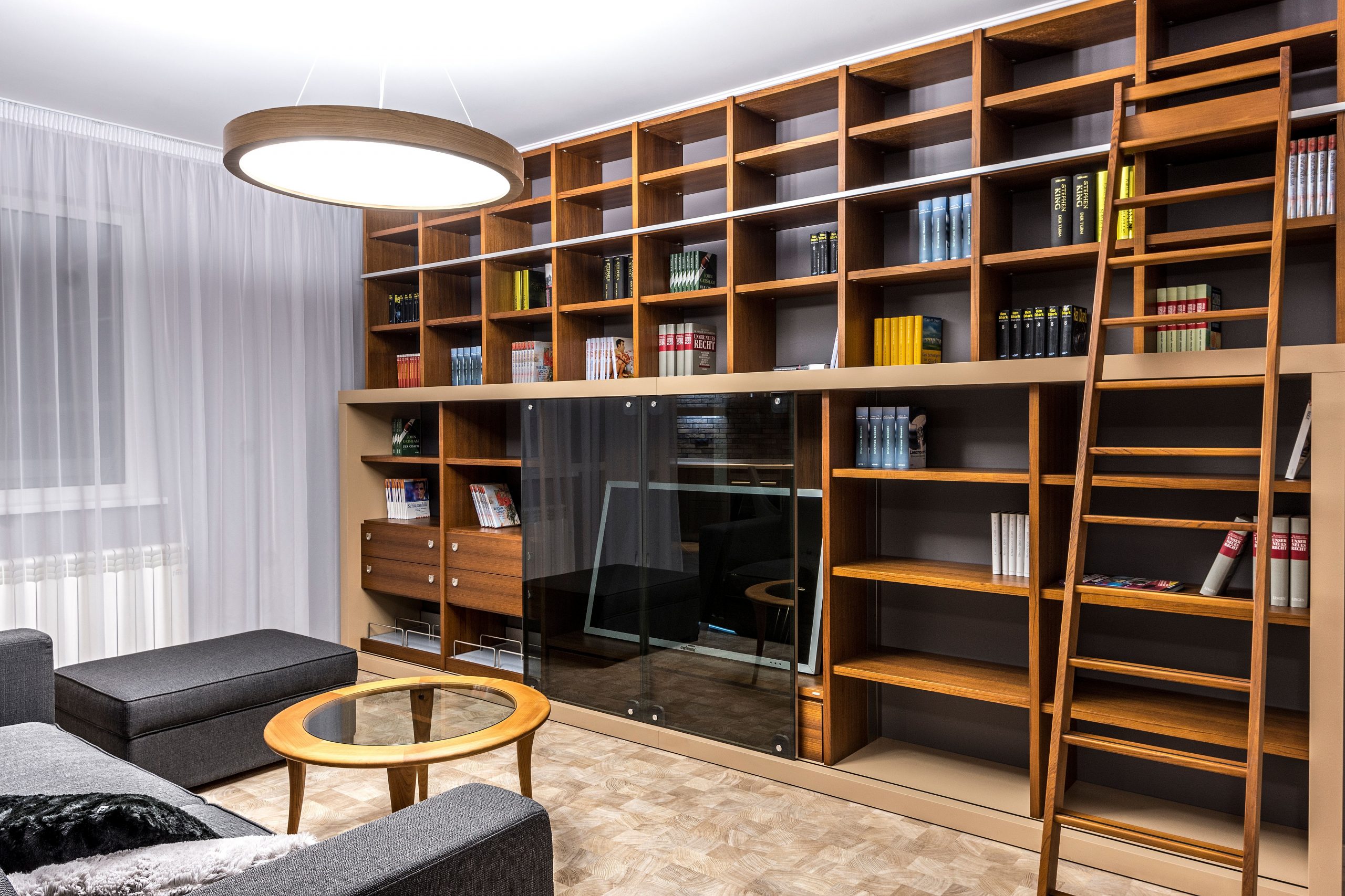 Stylish living room with wooden bookshelves and gray furniture, illuminated by a modern ceiling light.