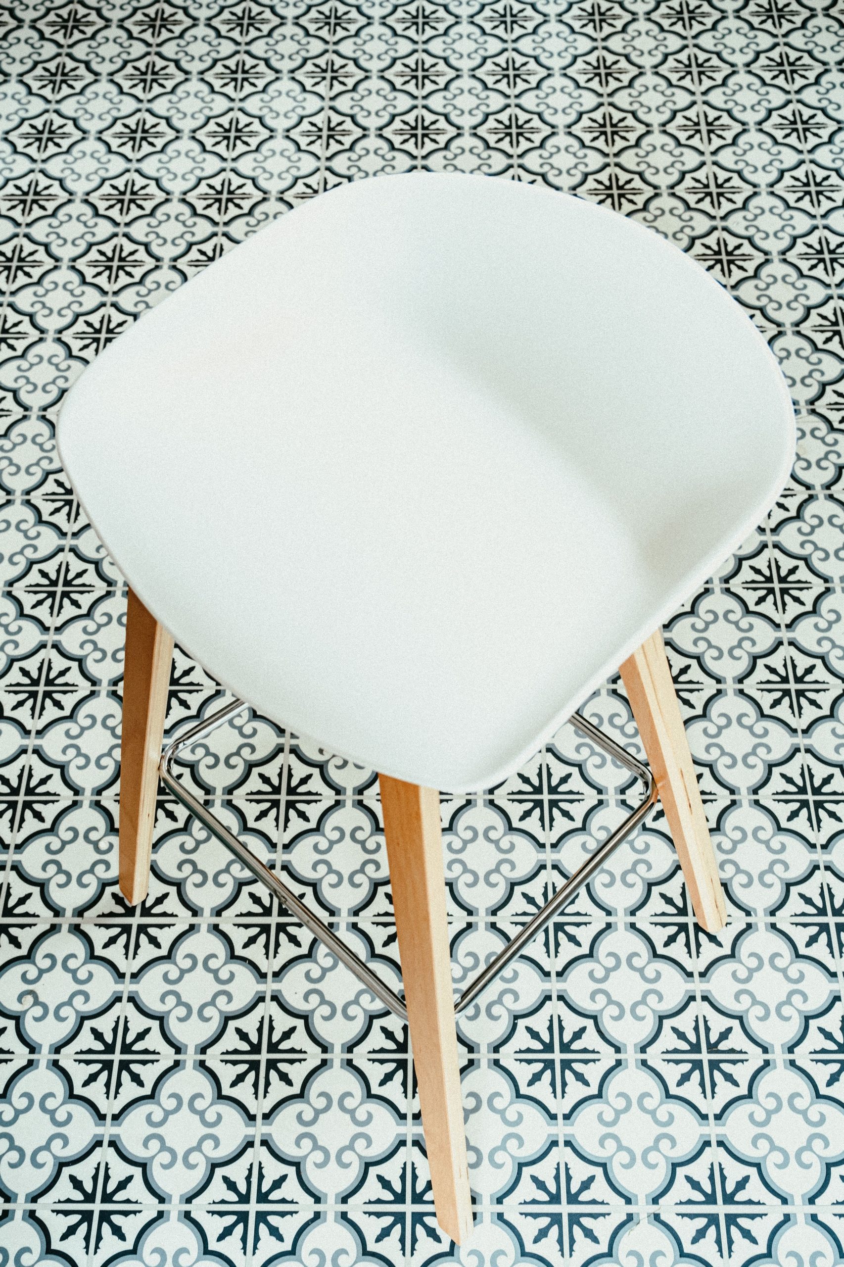 Stylish white chair with wooden legs on a decorative tiled floor, offering a minimalist aesthetic.