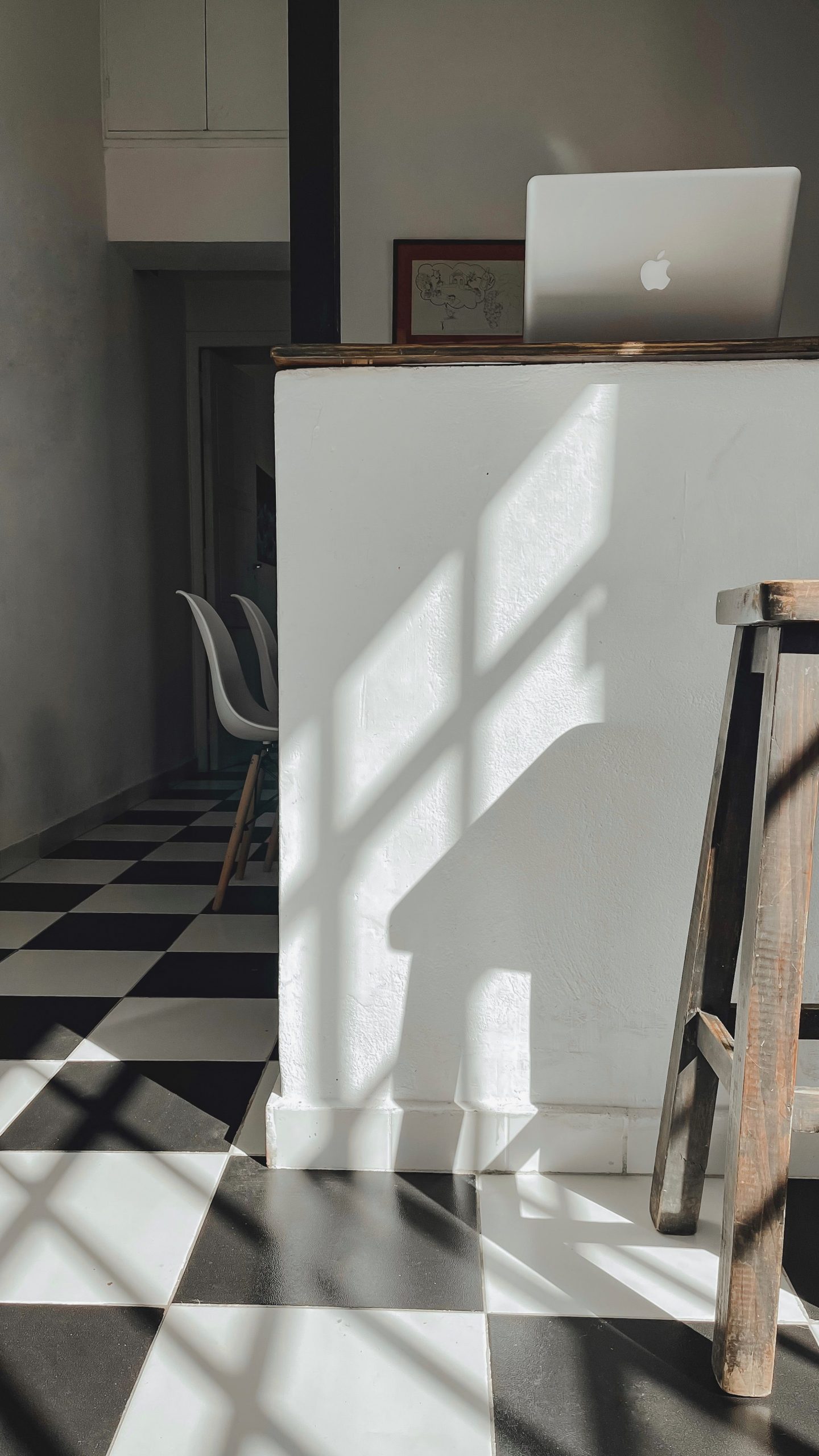 Sun-drenched kitchen with black and white checkered floor and laptop on counter.