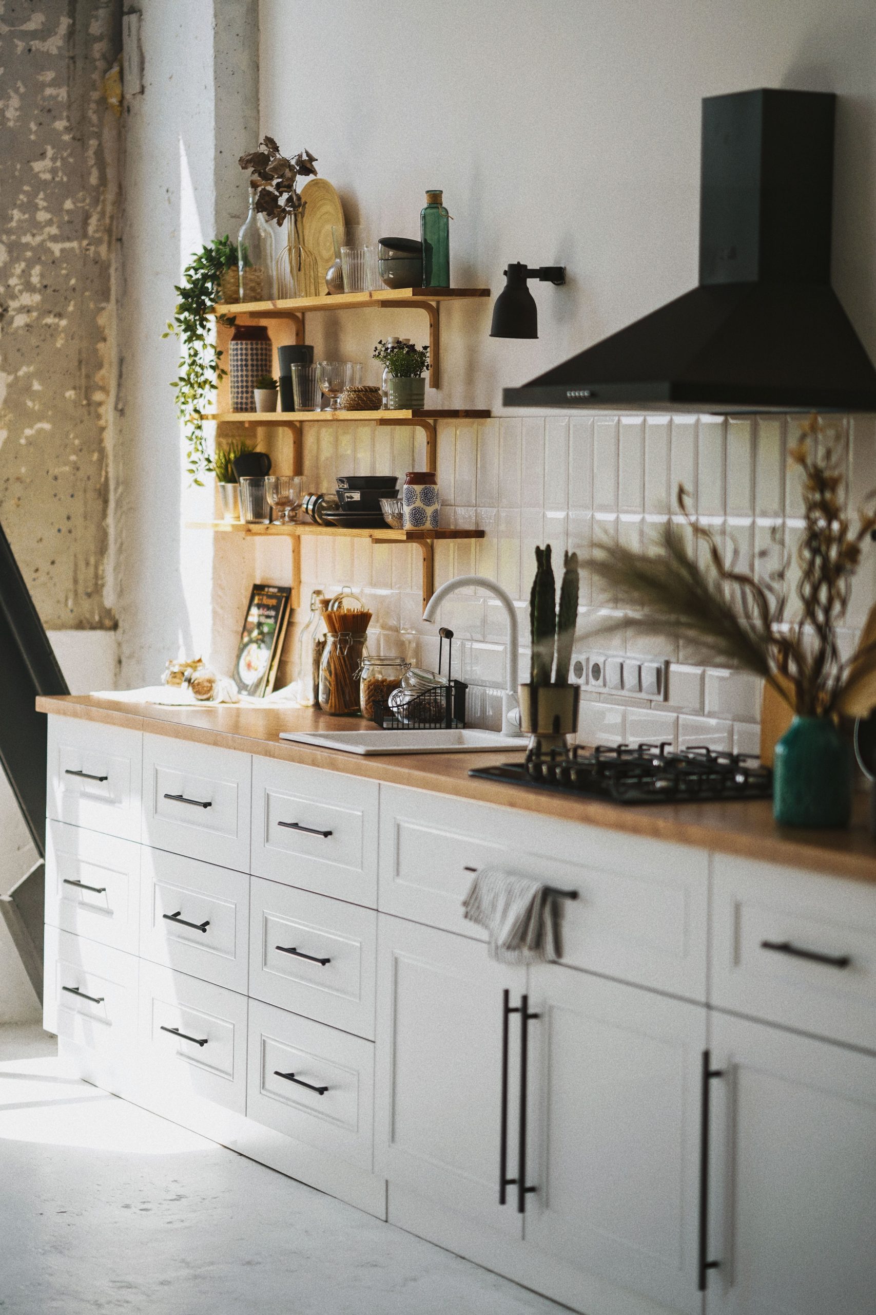 Sunlit modern kitchen in Scandinavian style with wooden shelves and white cabinetry.