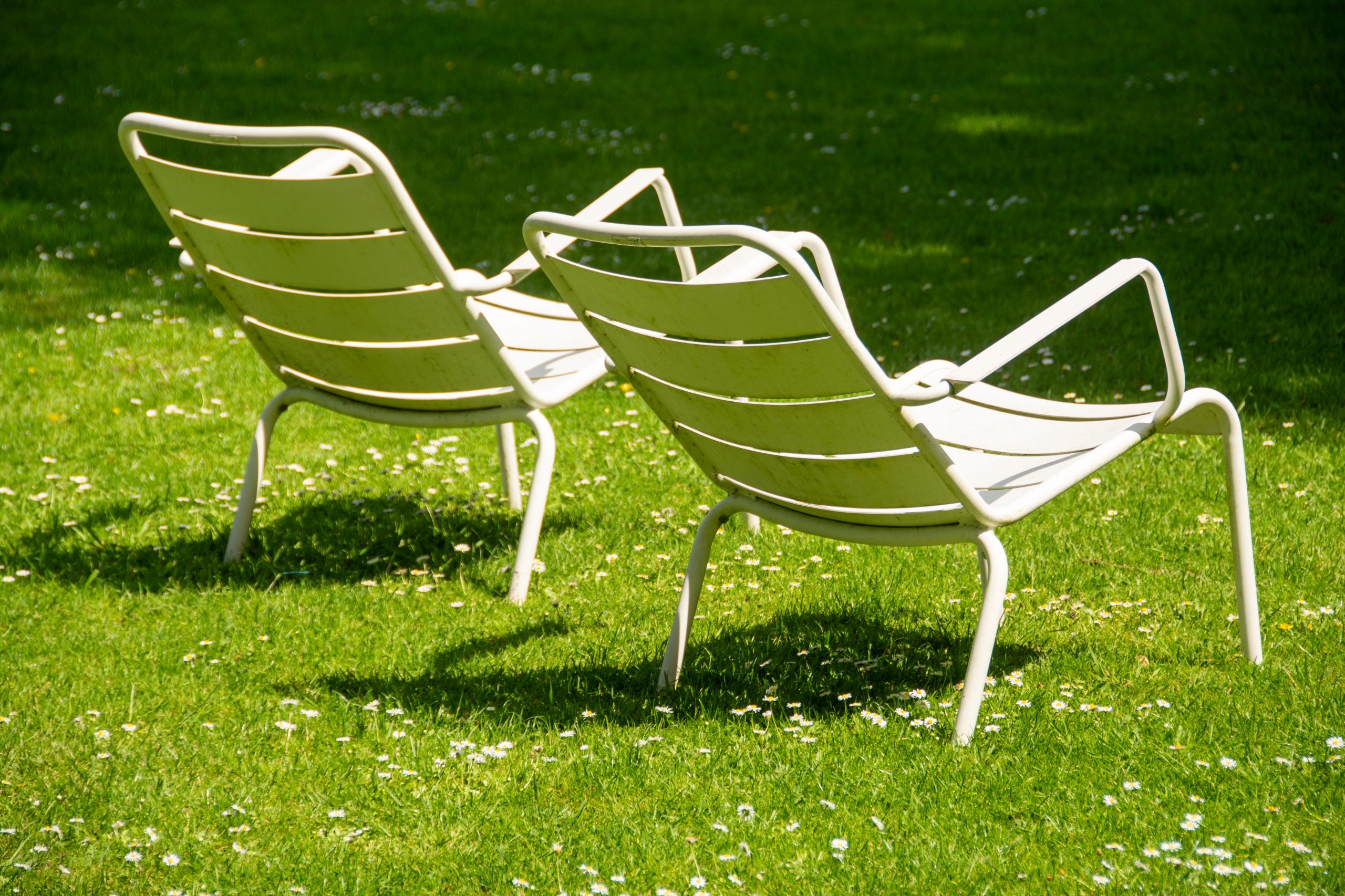 Two white metal chairs on a vibrant green lawn under sunlight.