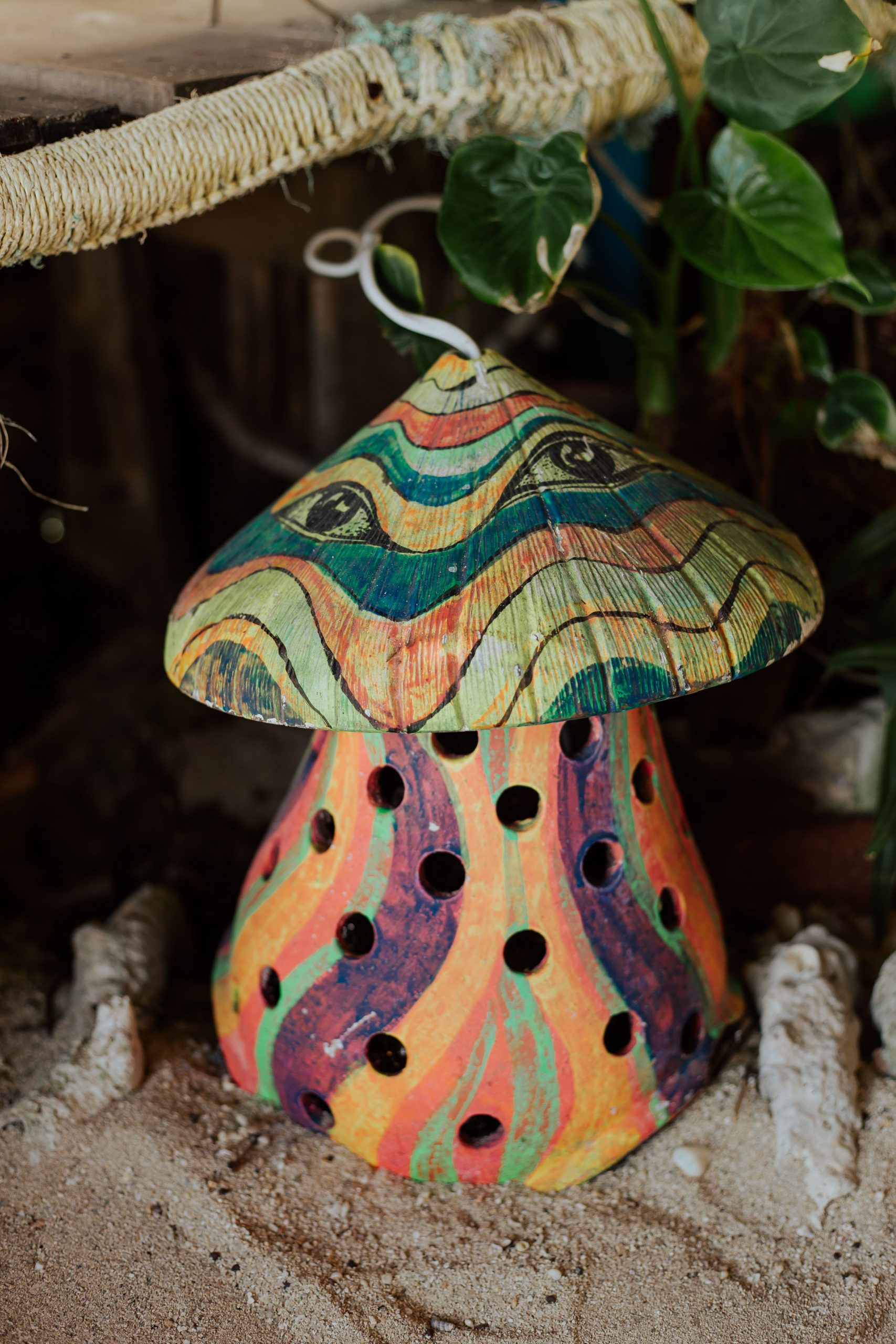 Vibrant mushroom-shaped garden figurine with colorful design among leaves and sand.
