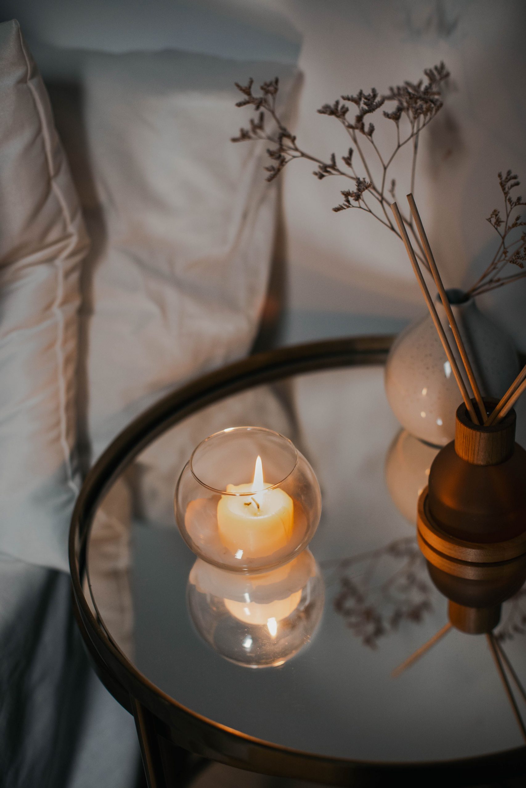Warm ambiance with a candle reflection on a glass table next to decorative vases and throw pillows.