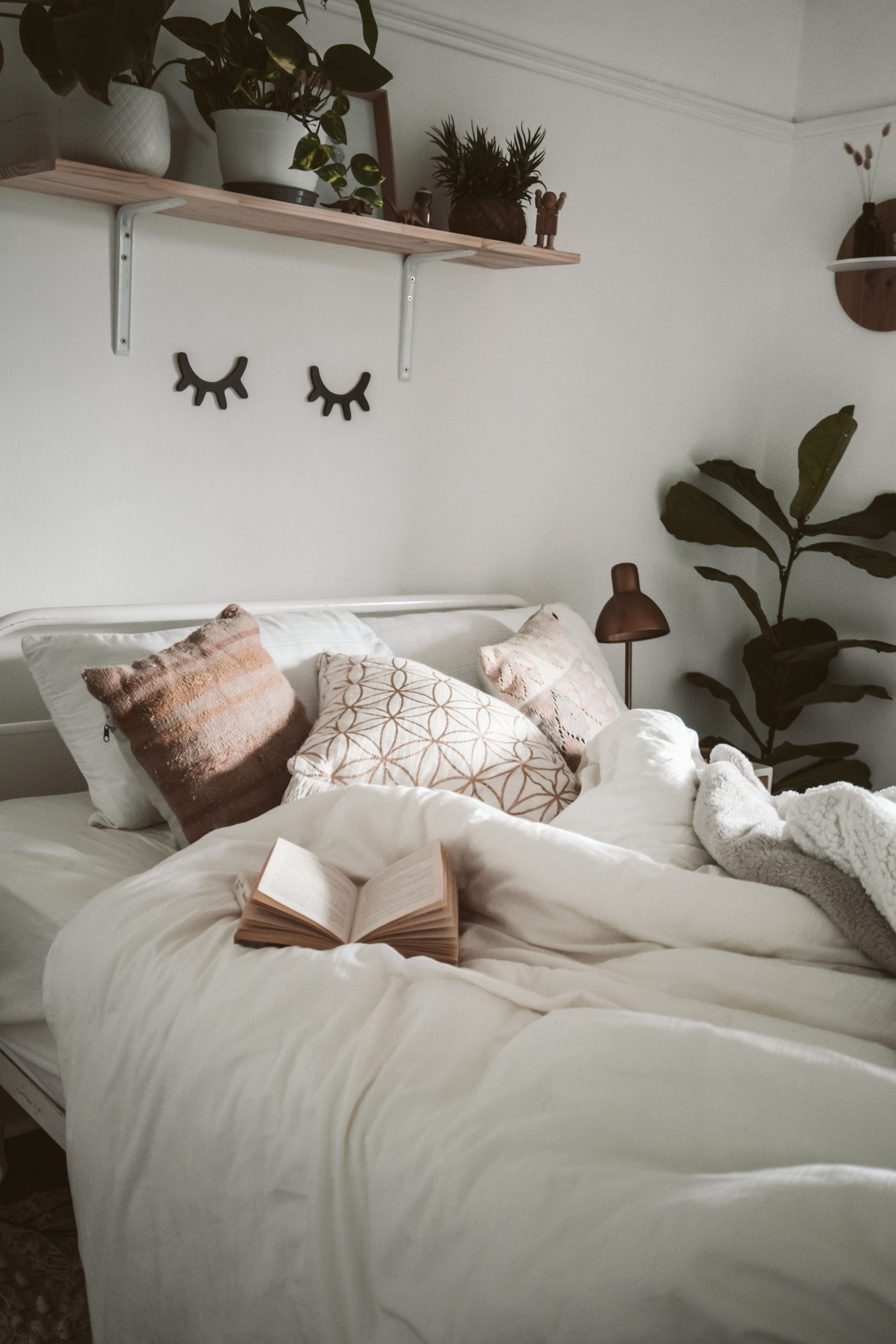 Warm and inviting bedroom setup with decorative pillows, plants, and an open book for a cozy ambiance.