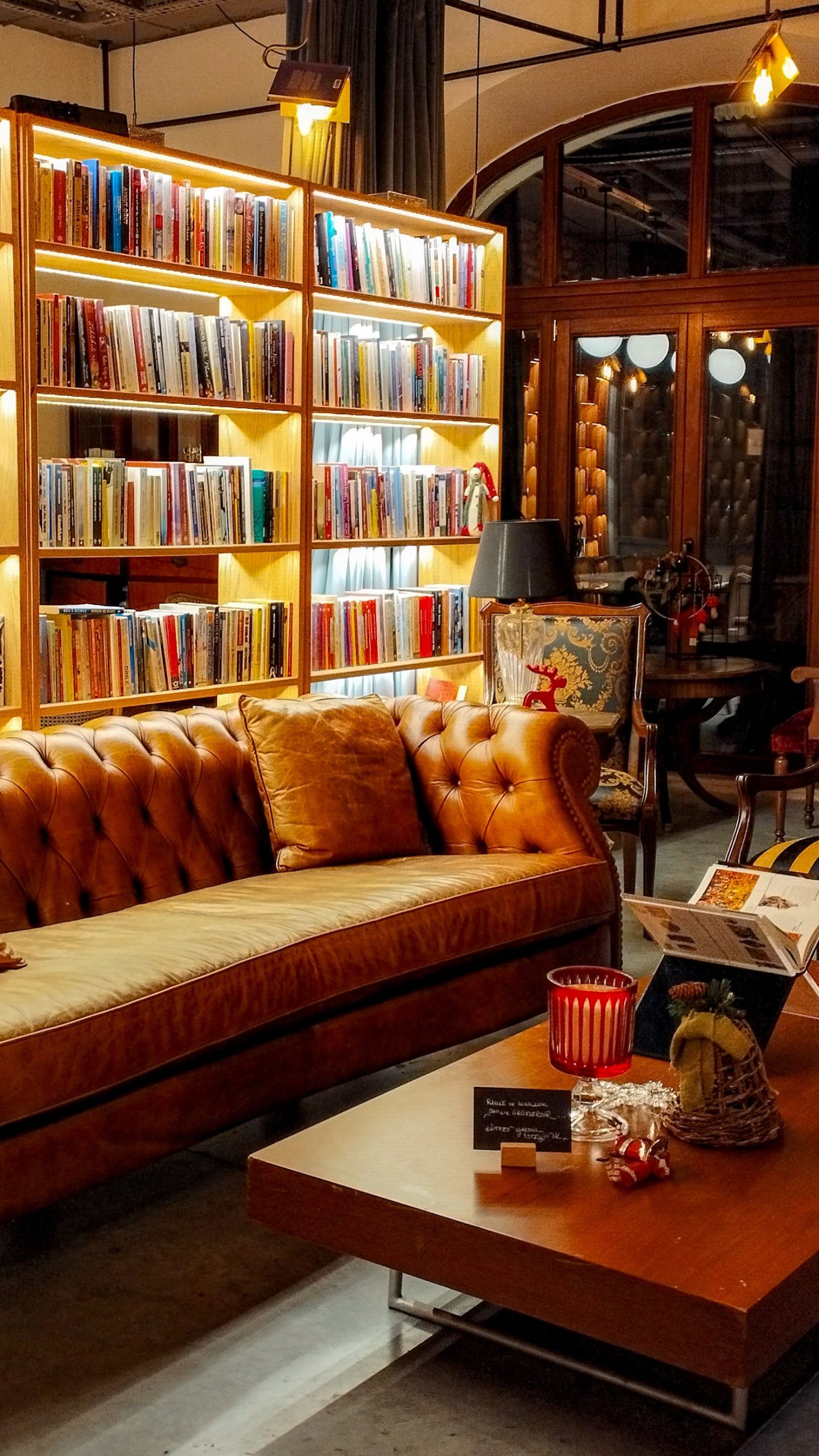 Warm library interior with bookshelves, leather sofa, and wooden table.