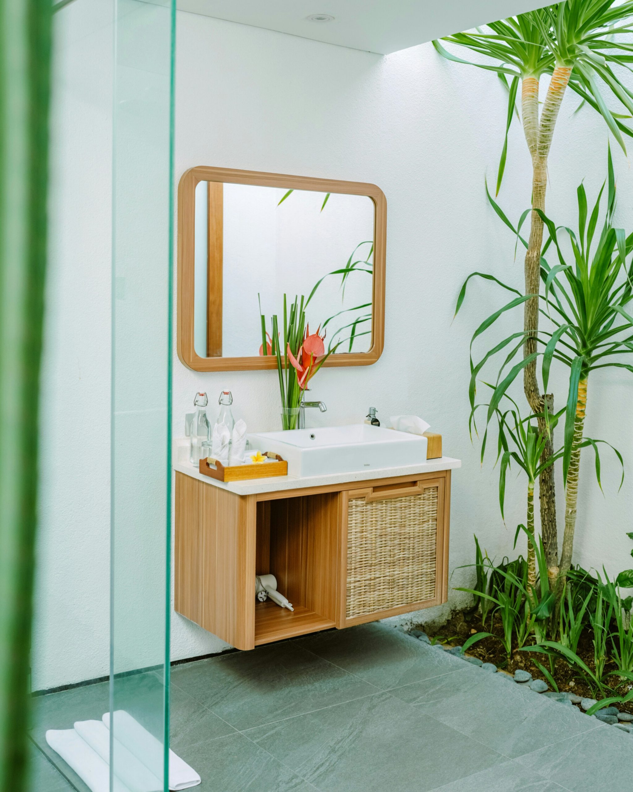 A beautifully designed outdoor bathroom with wooden sink, tropical plants, and natural light — reflecting Bali's signature resort aesthetic and relaxed, nature-inspired luxury.