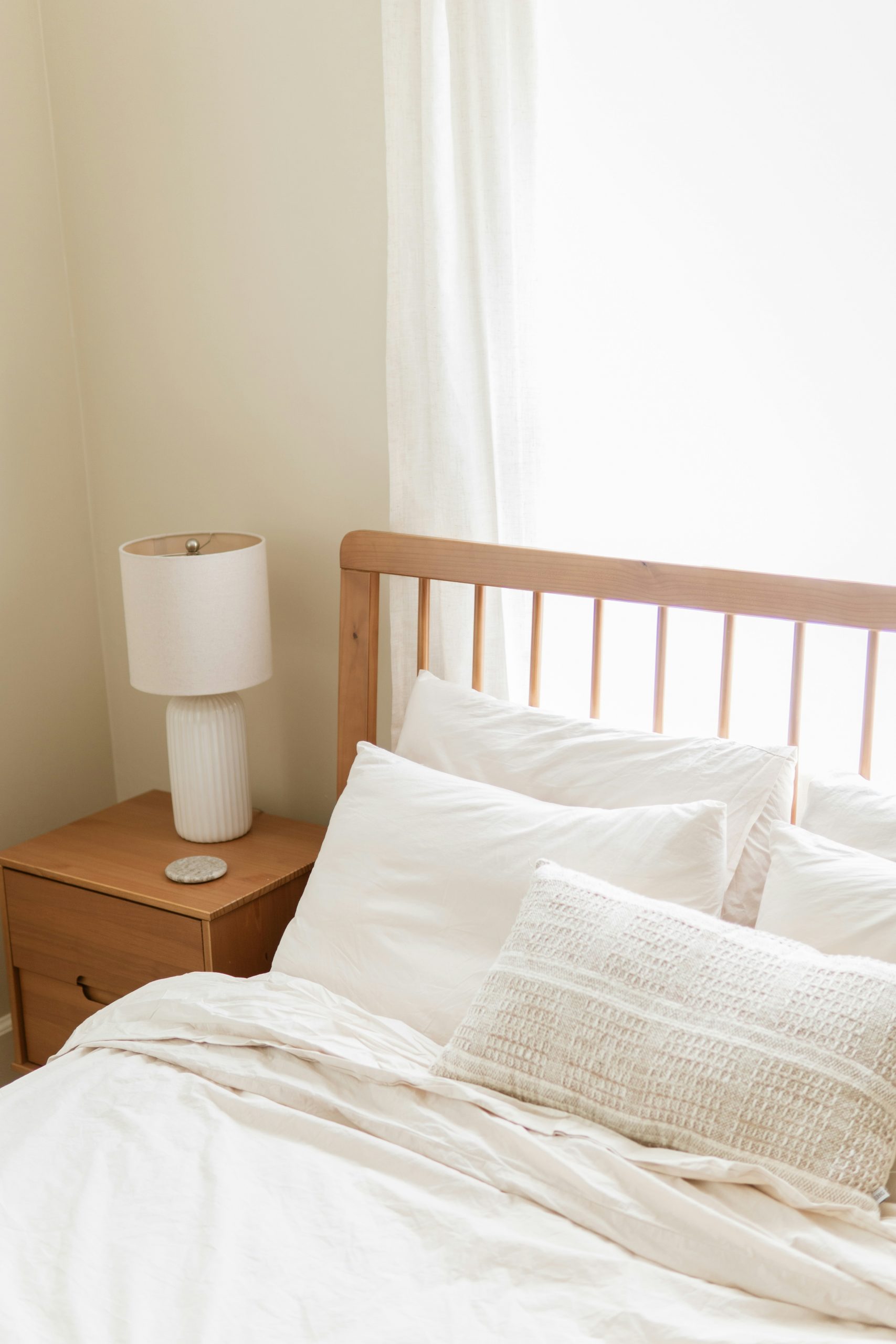 A bright bedroom with white bedding, wooden headboard, and nightstand.