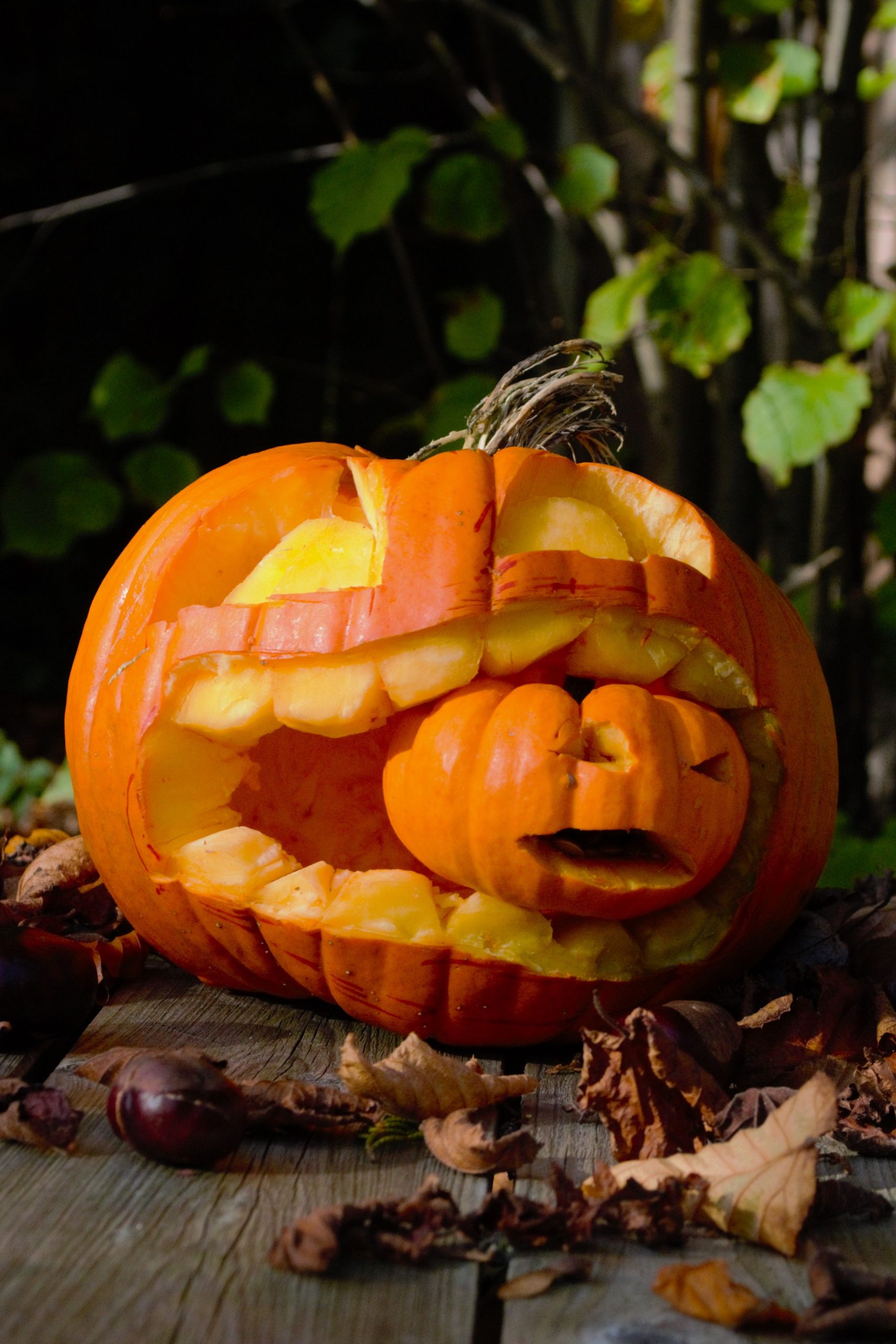 A carved Halloween pumpkin with a comical face on a rustic wooden table surrounded by fall leaves.