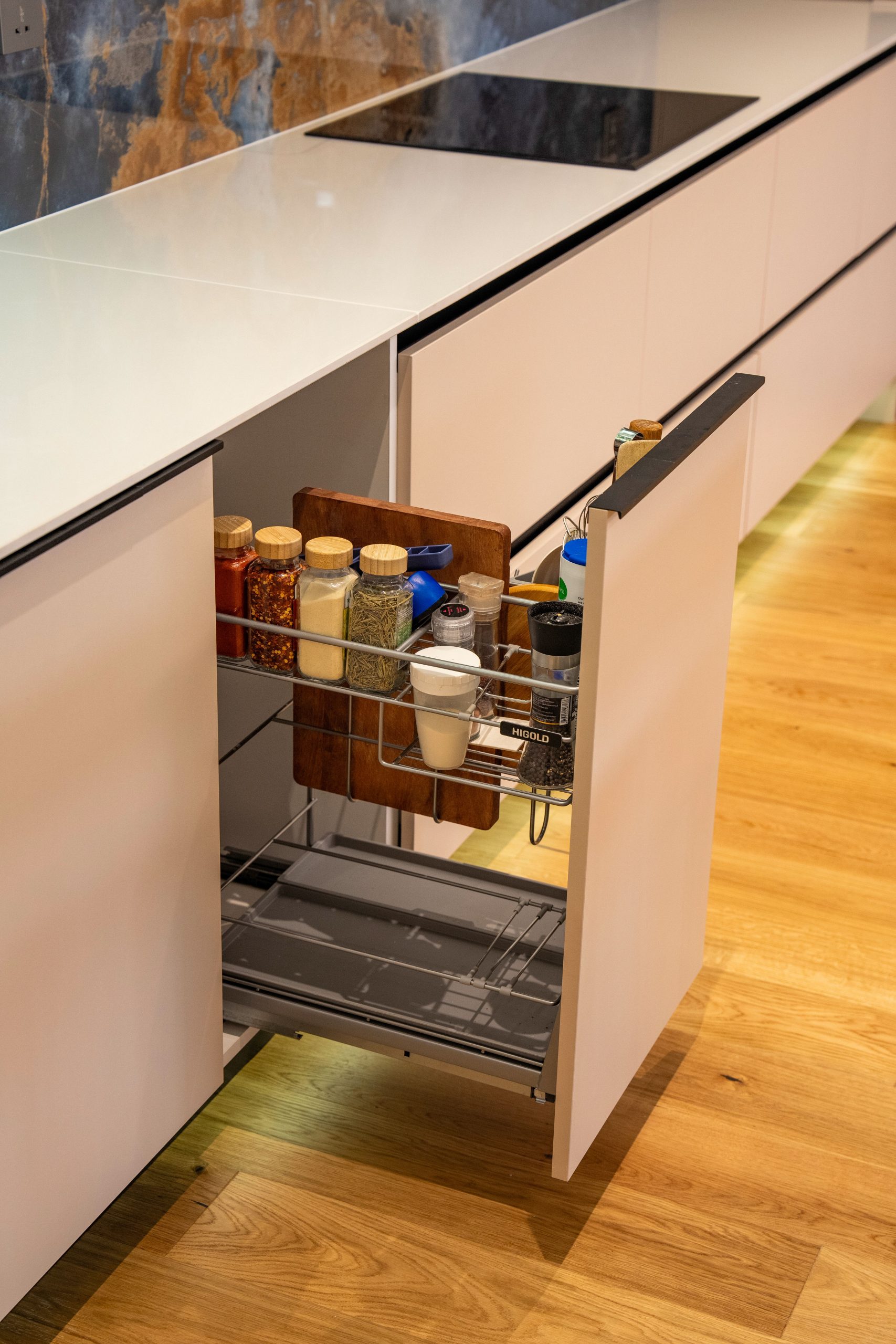 A contemporary kitchen featuring a pull-out spice rack with colorful spices and wooden cutting board.