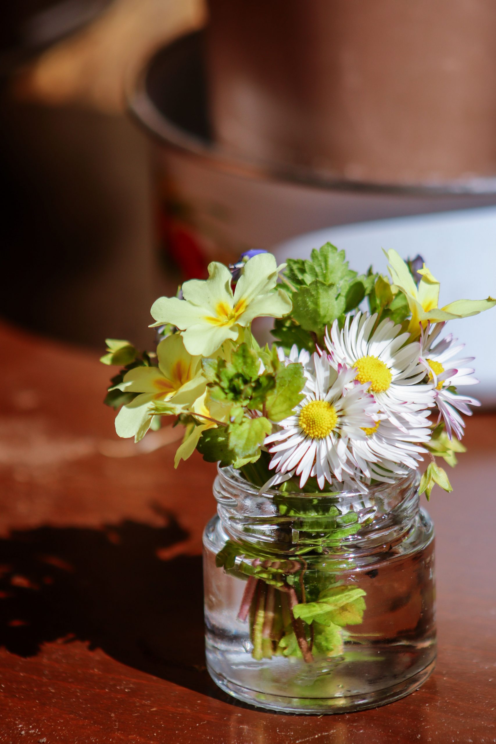 A delightful arrangement of wildflowers in a small glass jar on a sunlit wooden table.