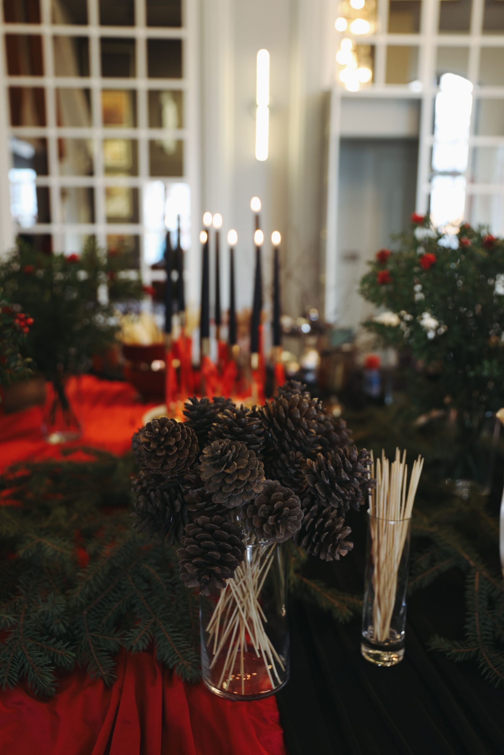 A festive holiday table setting featuring pinecones, candles, and greenery indoors.