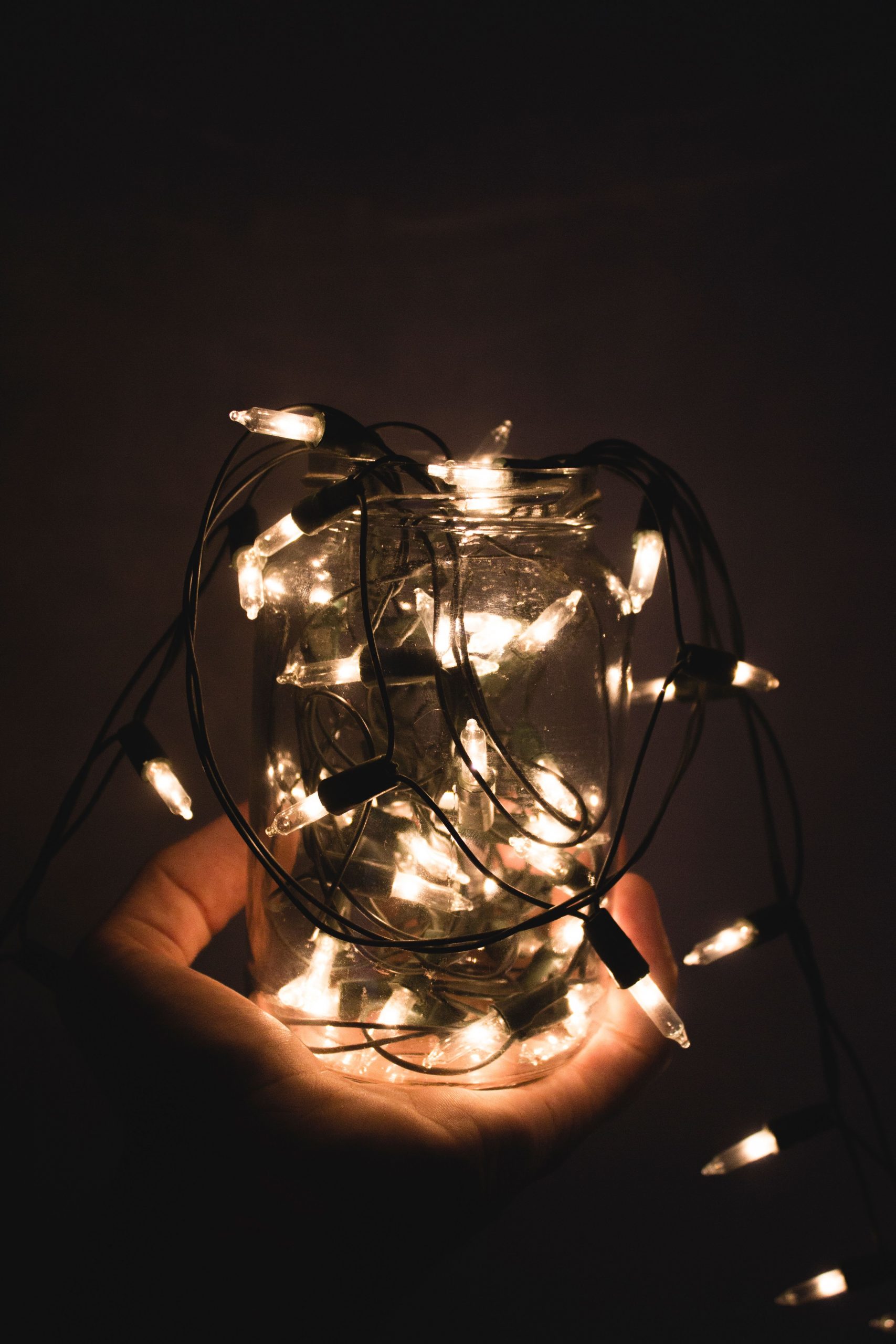 A glass jar full of glowing Christmas lights held in a hand, creating a warm ambiance.