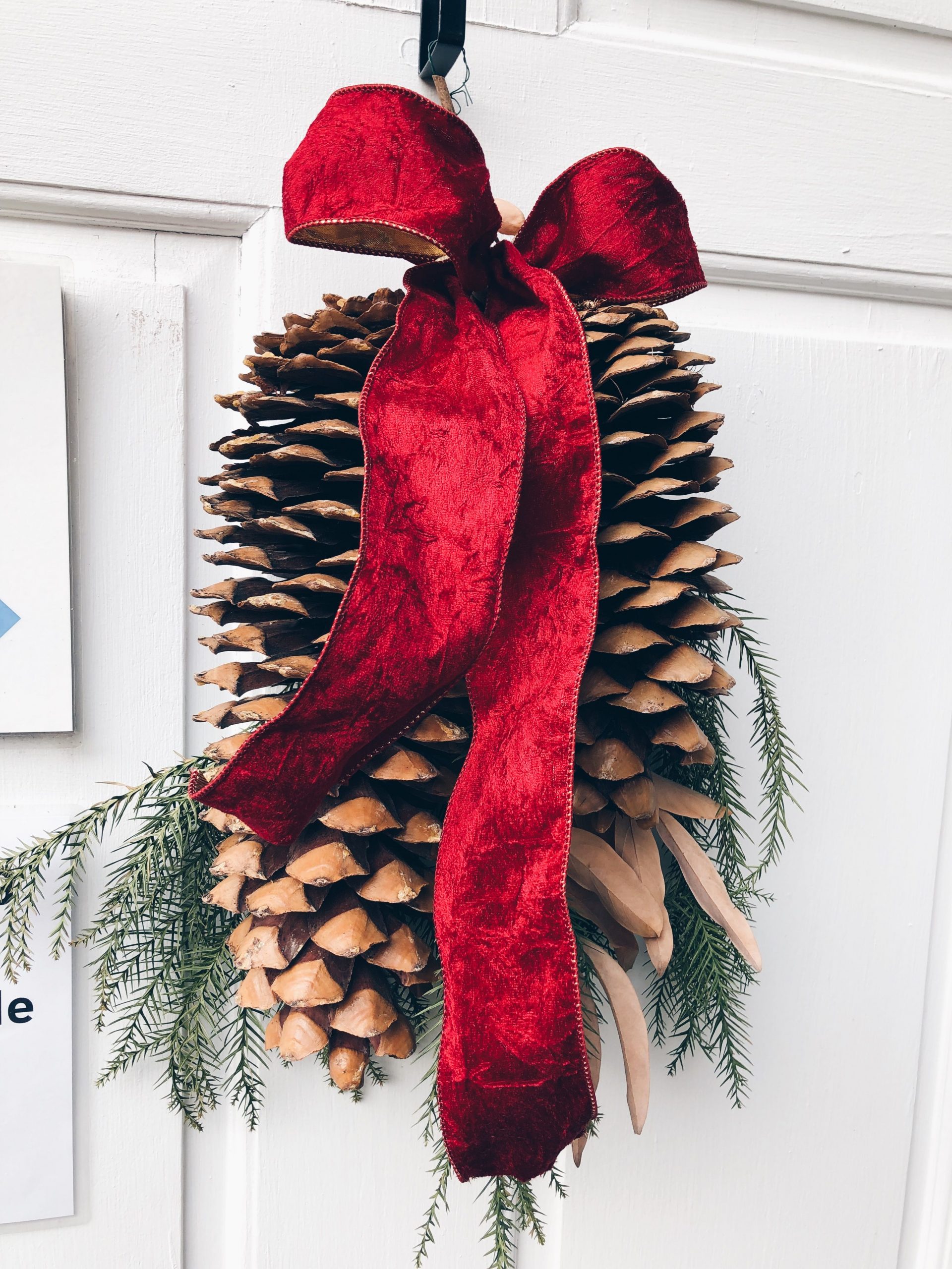 A large pinecone adorned with a red ribbon and greenery, perfect for Christmas decor.