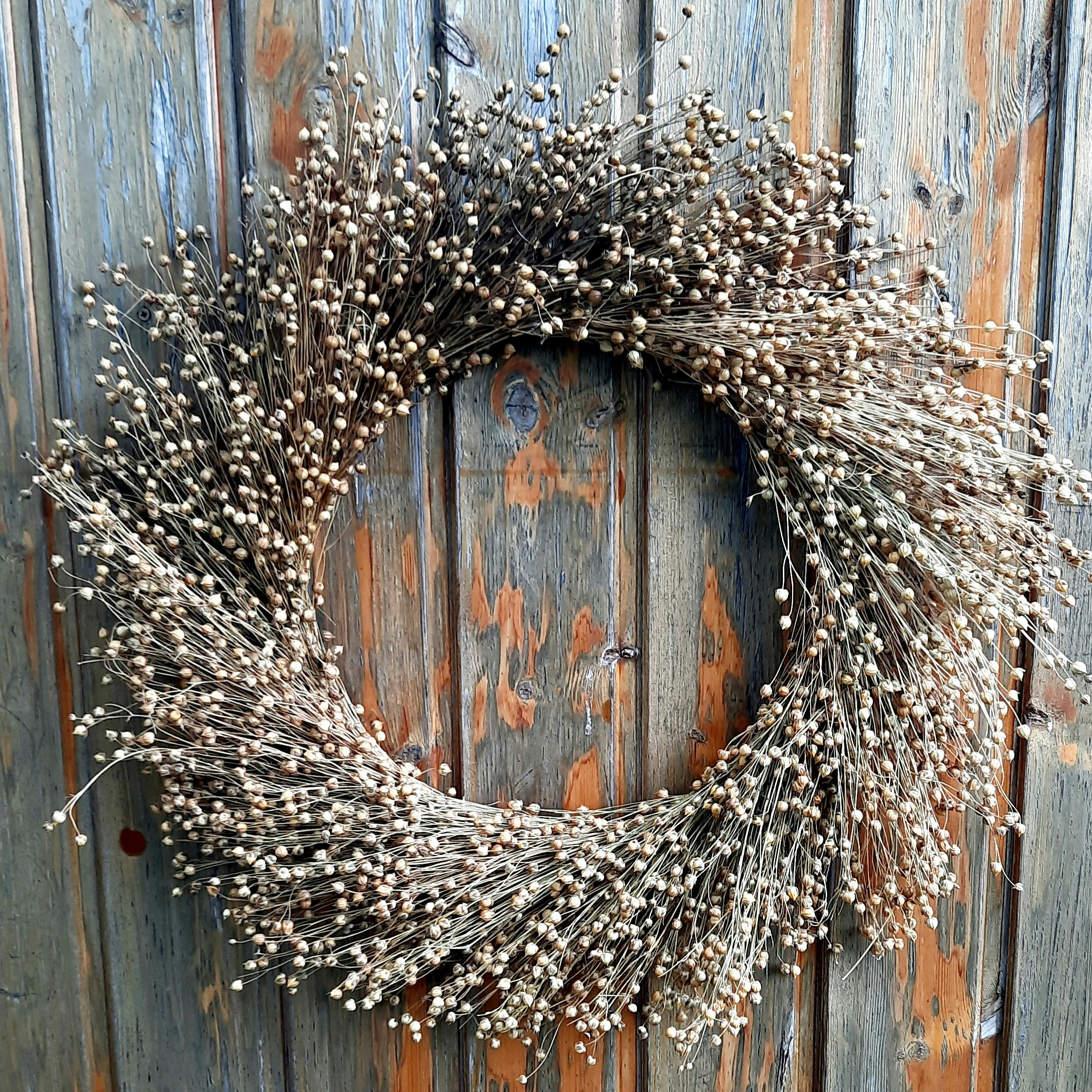 A rustic dried flower wreath hangs on a wooden door.
